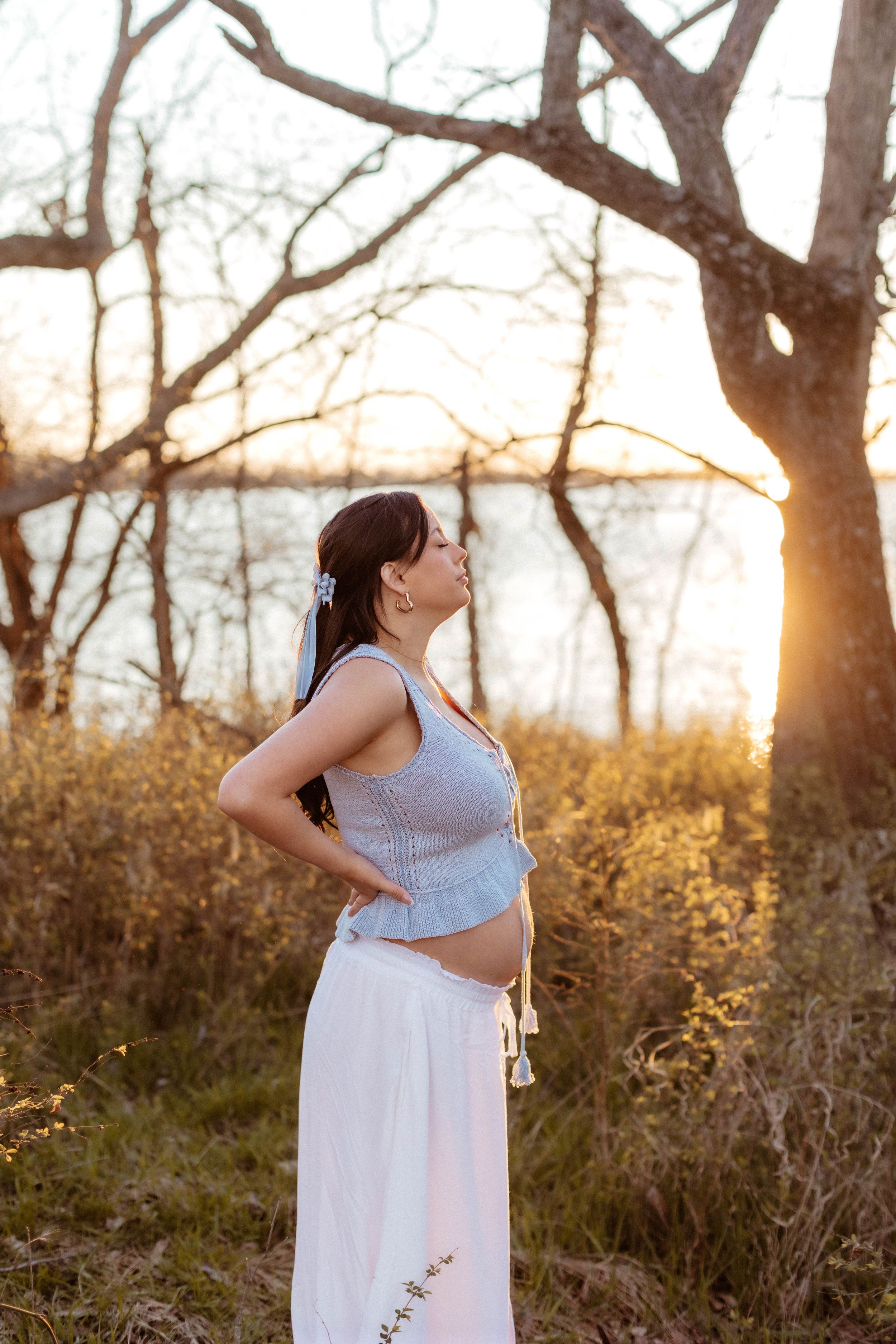 A pregnant woman looks up with her eyes closed and hands on her hips during a golden hour maternity photo session in Kansas City.