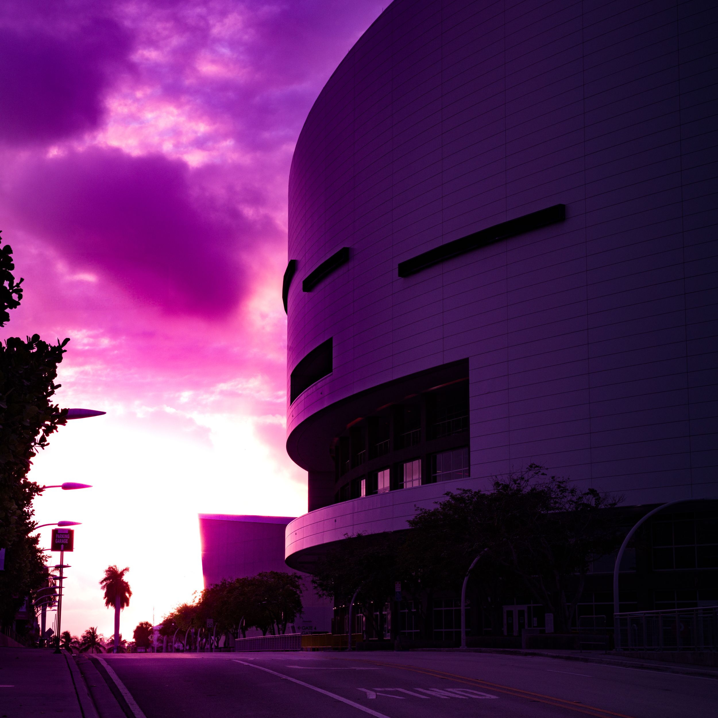 Architectural photo of a curved modern building against a dramatic purple sunset sky