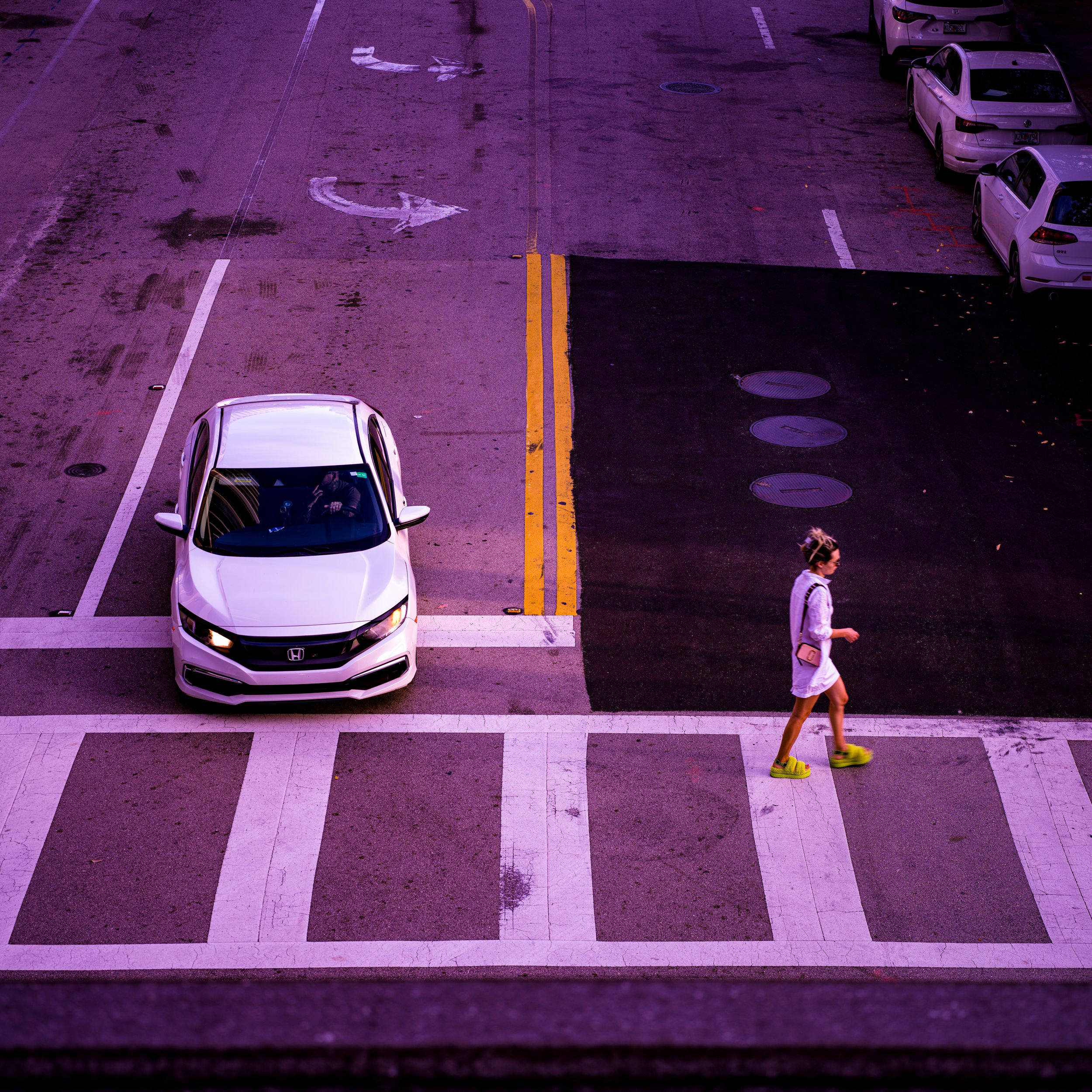 High-angle urban photo of a street crosswalk with a car and pedestrian in purple tones