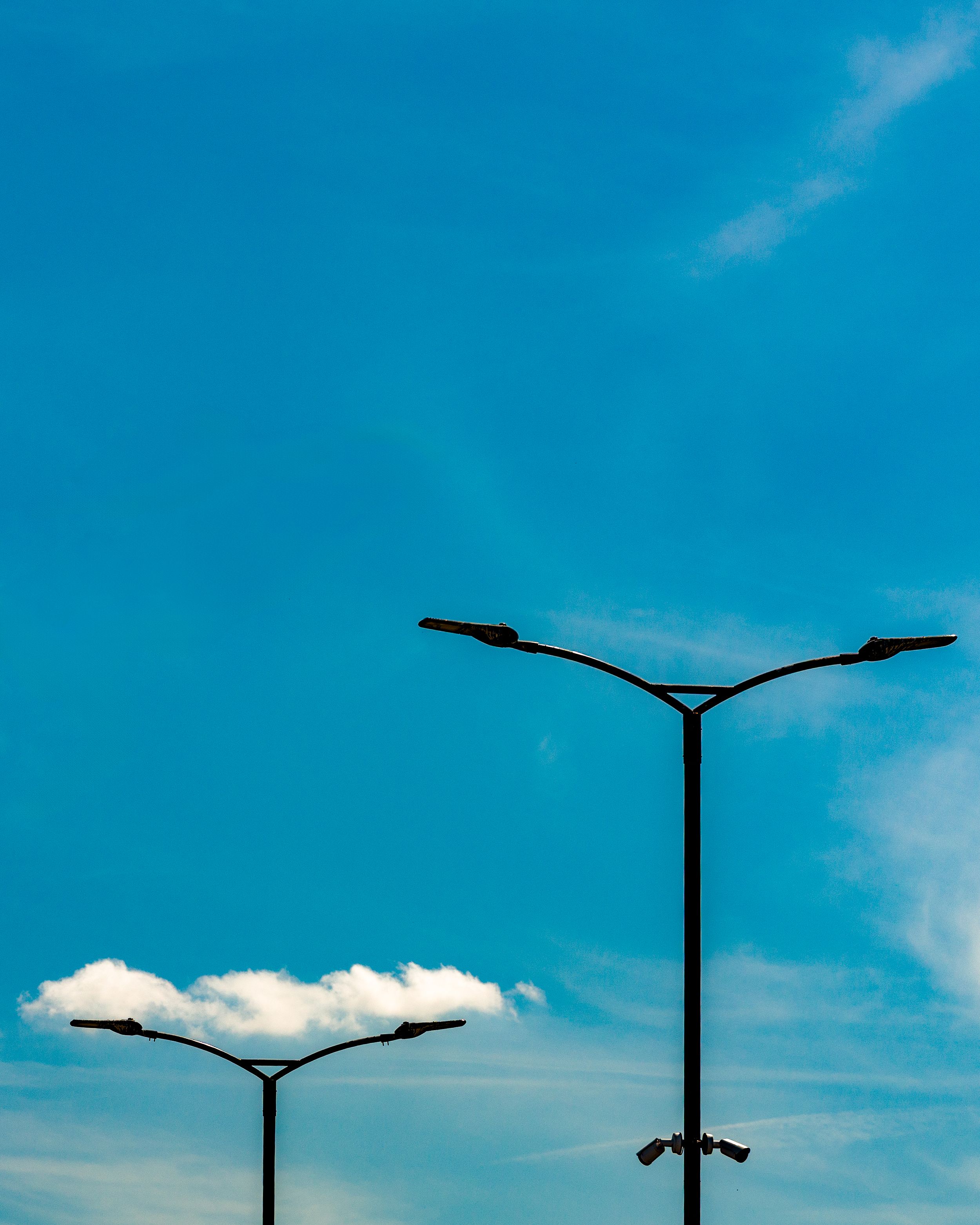 Minimalist photo of a street lamp against a blue sky with a cloud below it