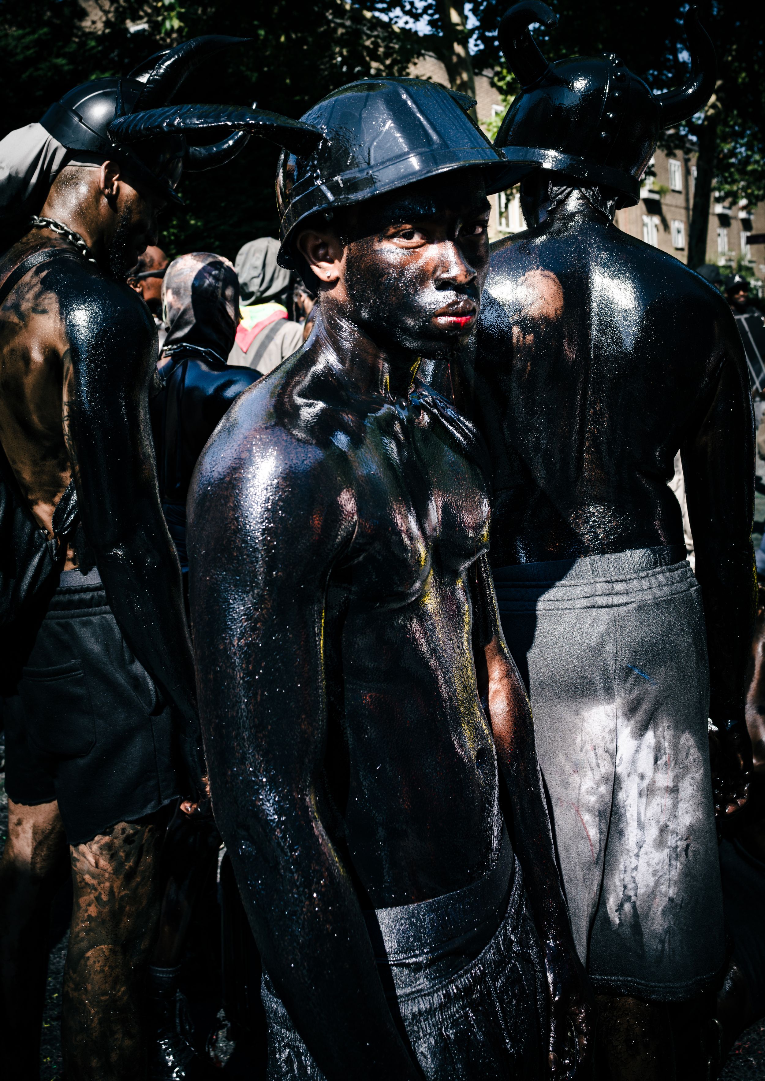 Street performance photography of people covered in black paint in dramatic sunlight