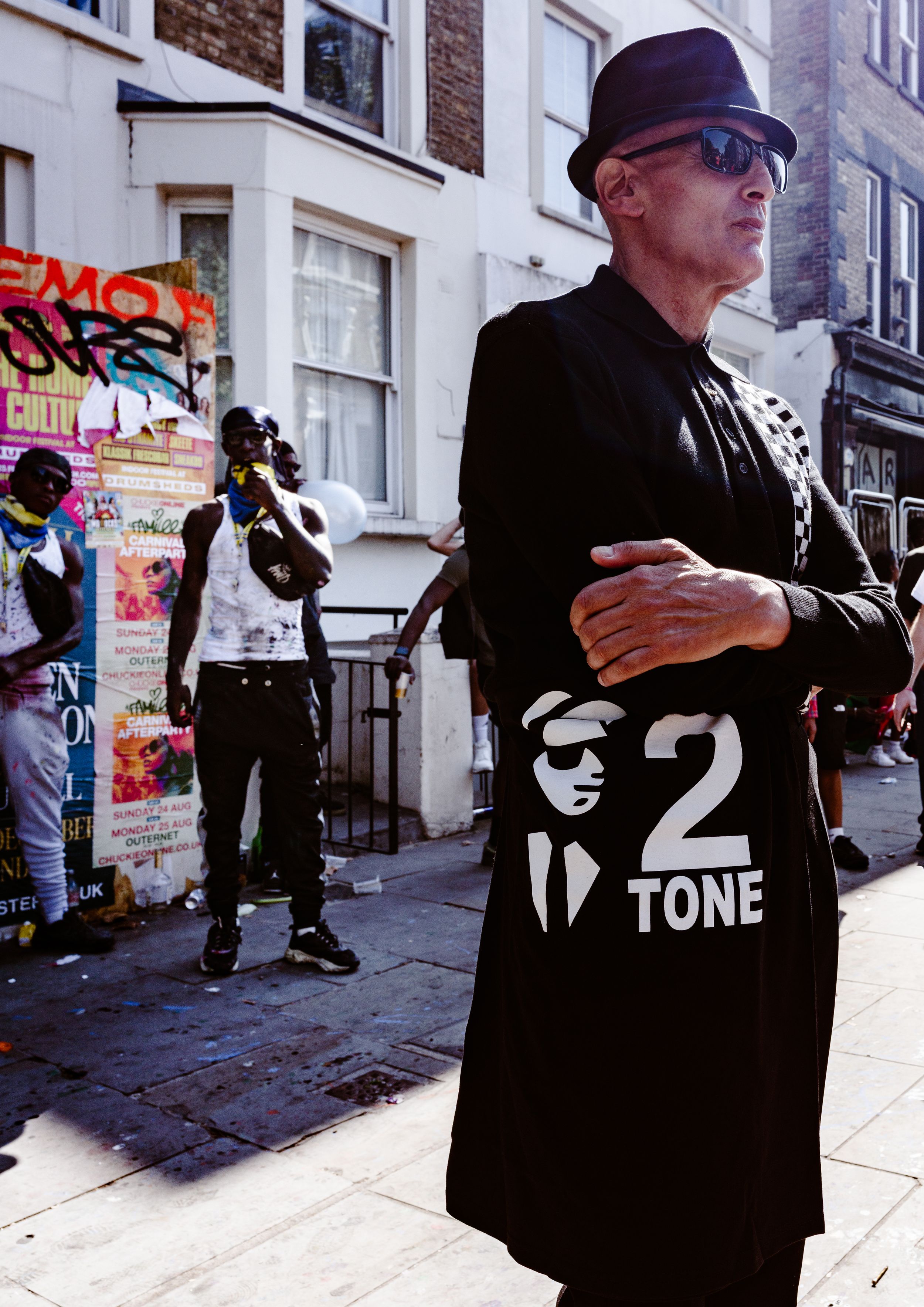 Street photography of a man in a black coat and bowler hat wearing a graphic jacket on an urban street