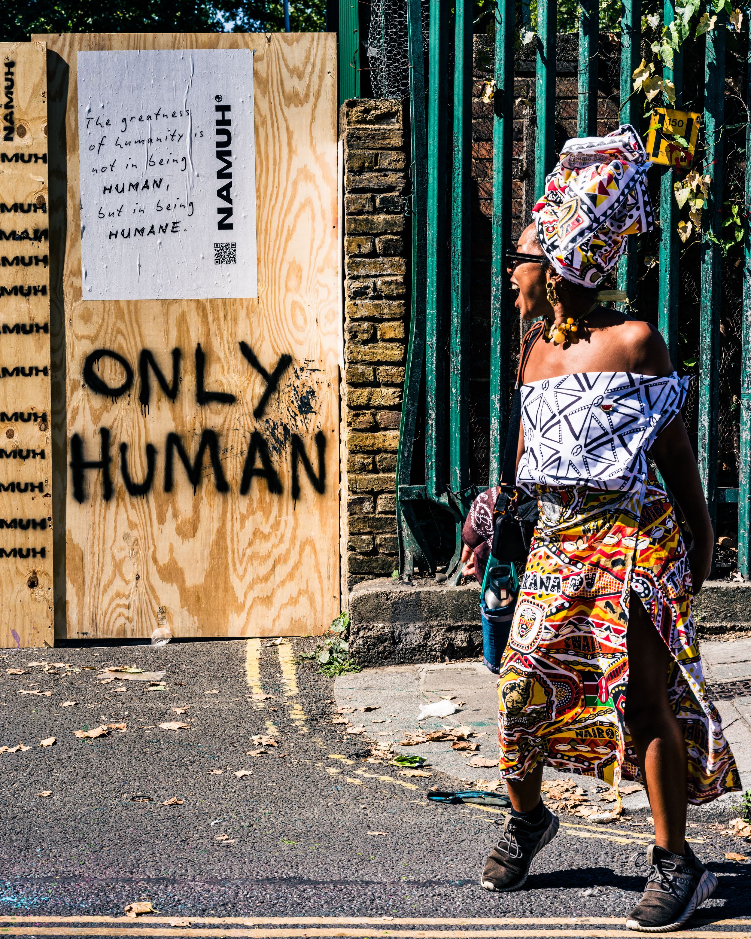 Street photography of a person walking past a sign reading Only Human on a wooden hoarding