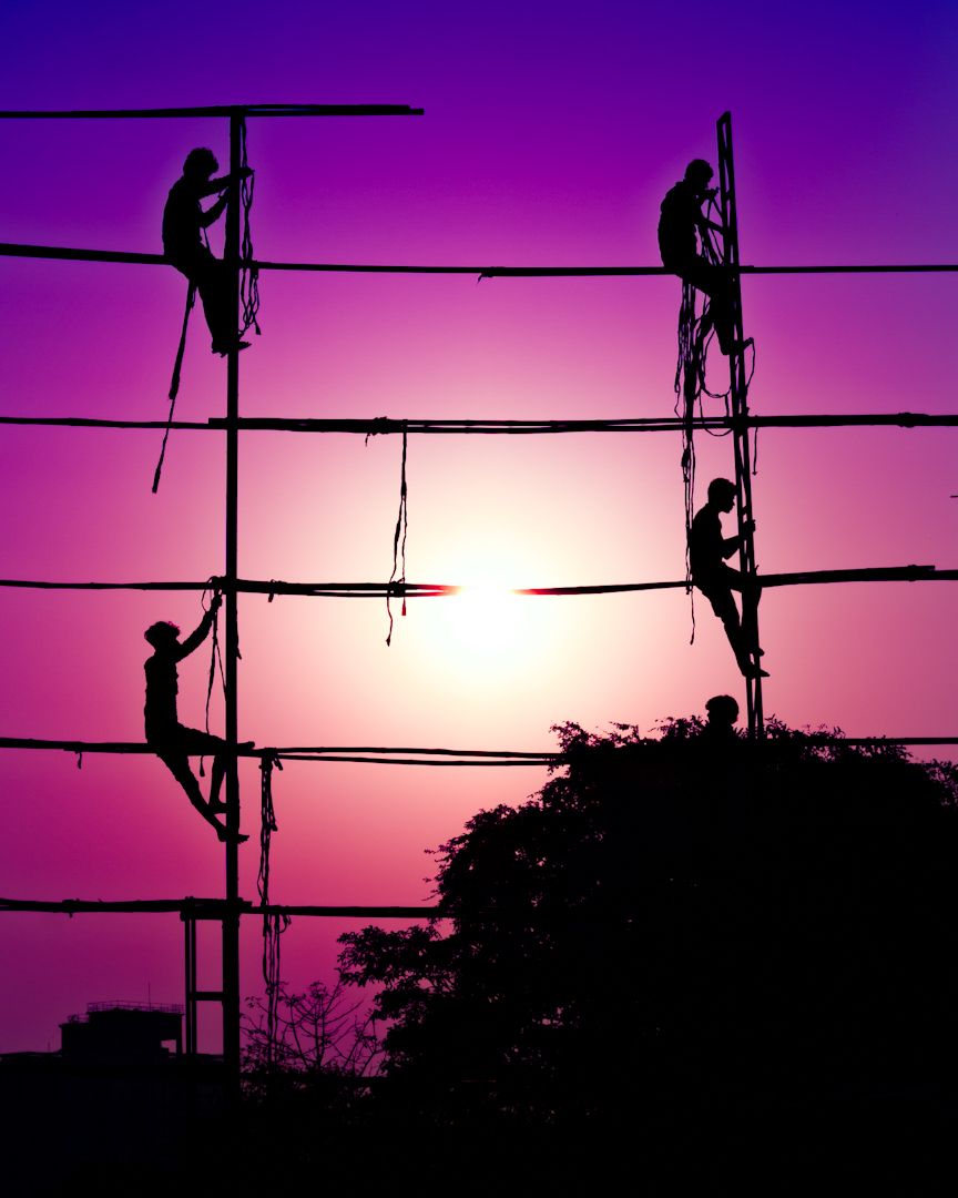 Silhouettes of workers on scaffolding against a purple sunset sky, street photography