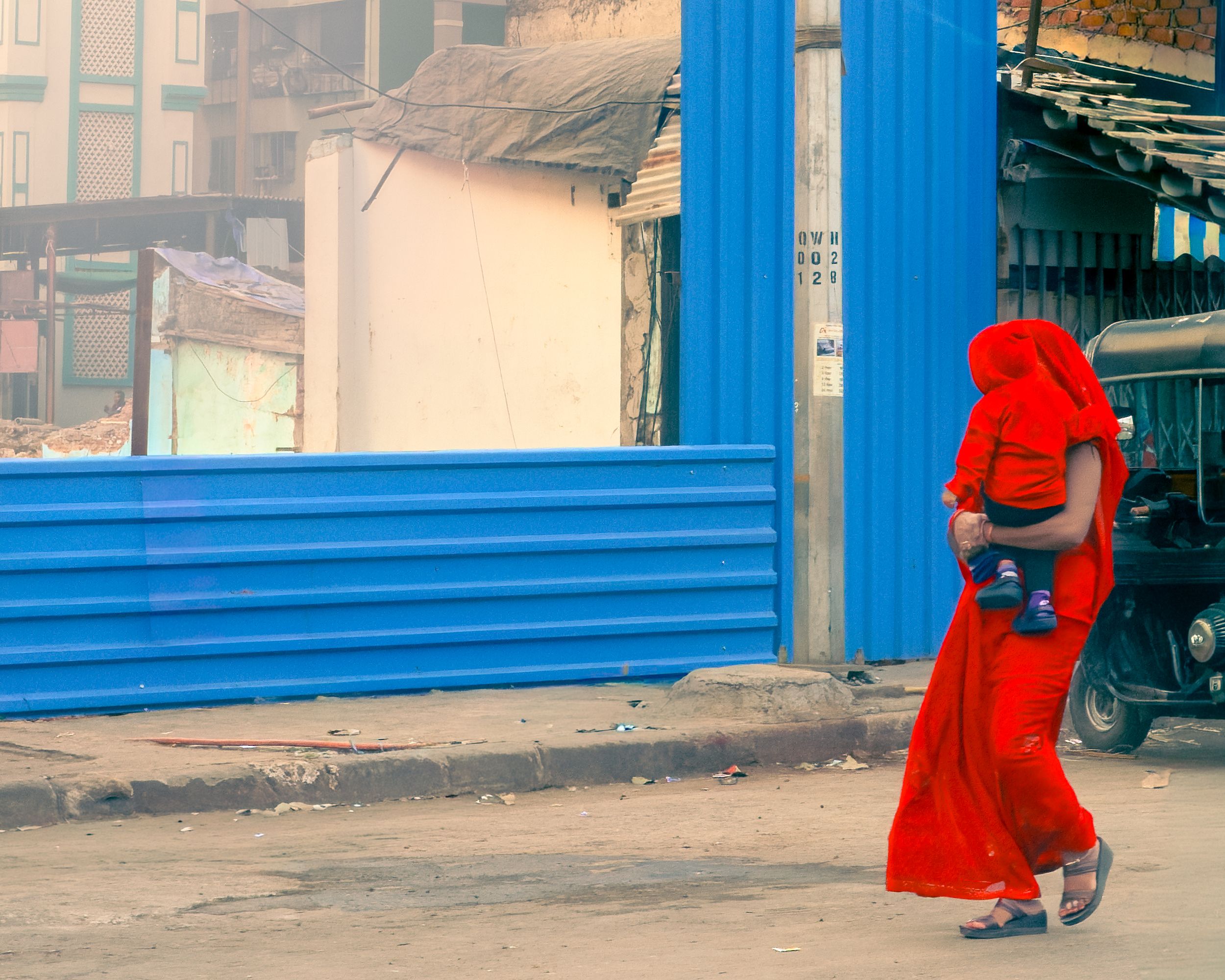 Street photography of a woman in a red outfit walking past a blue wall