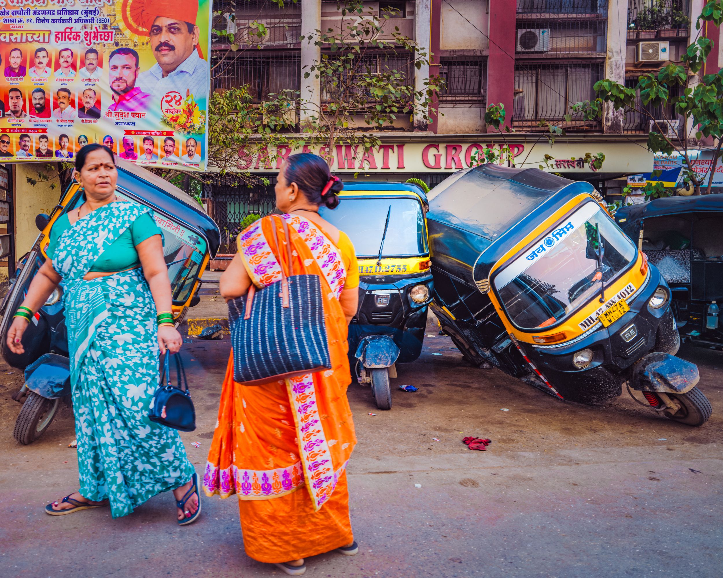 Street photography of two women in colourful traditional saris walking past auto-rickshaws