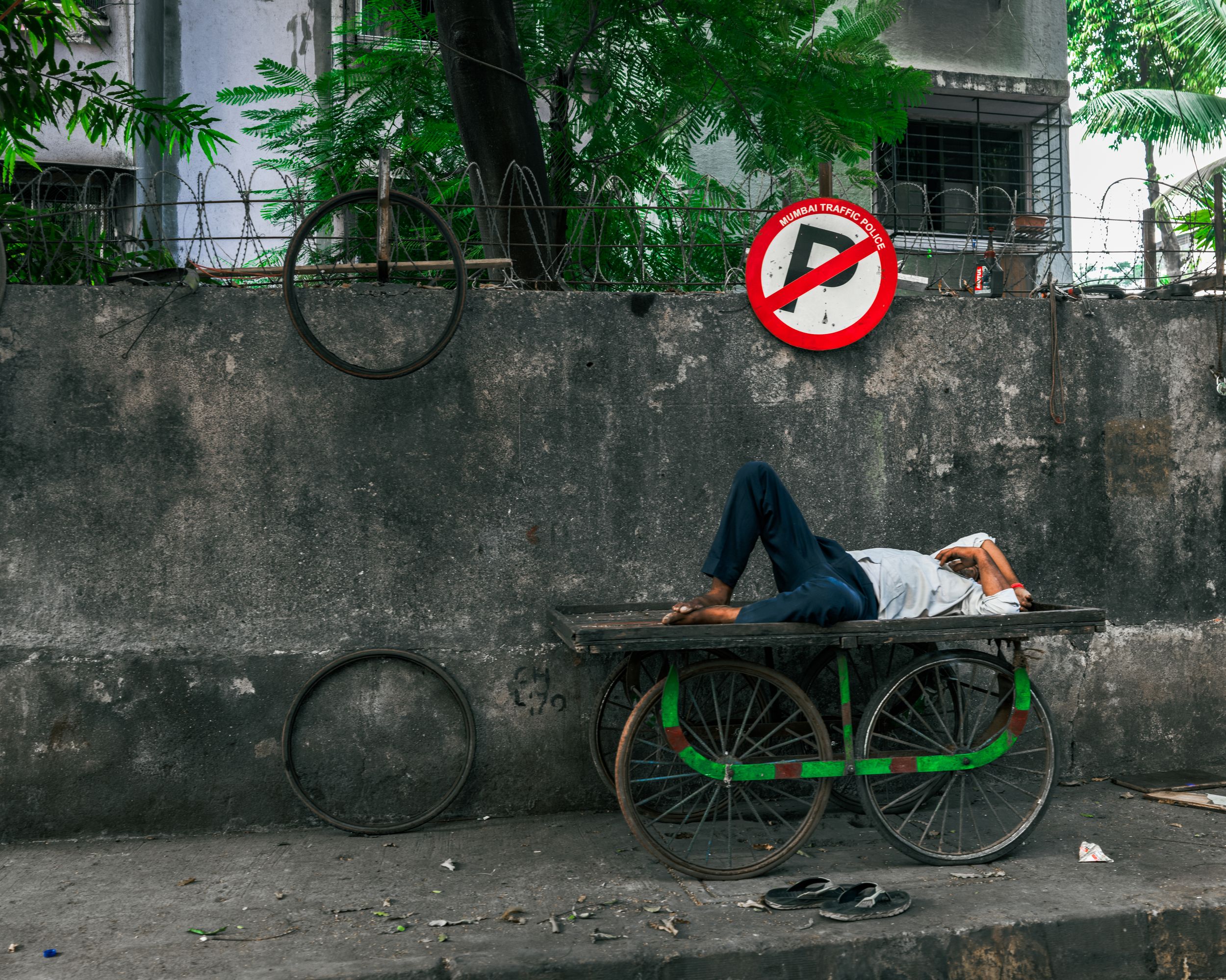 Street photography of a person resting on a bicycle cart beneath a no-entry sign
