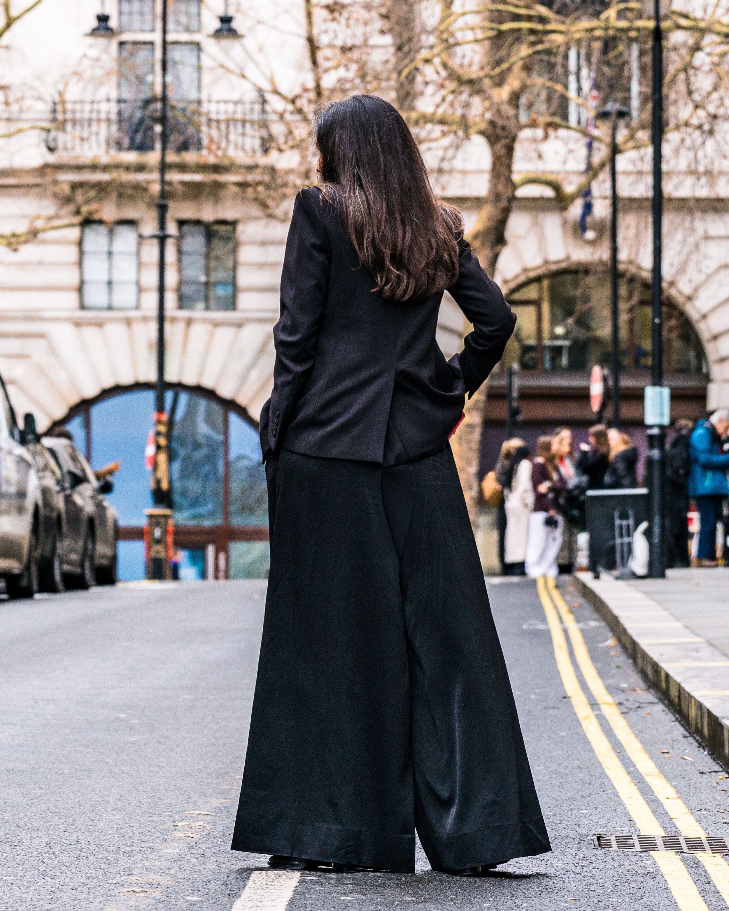 Street photography of a woman in a long black coat standing on a city street near an archway