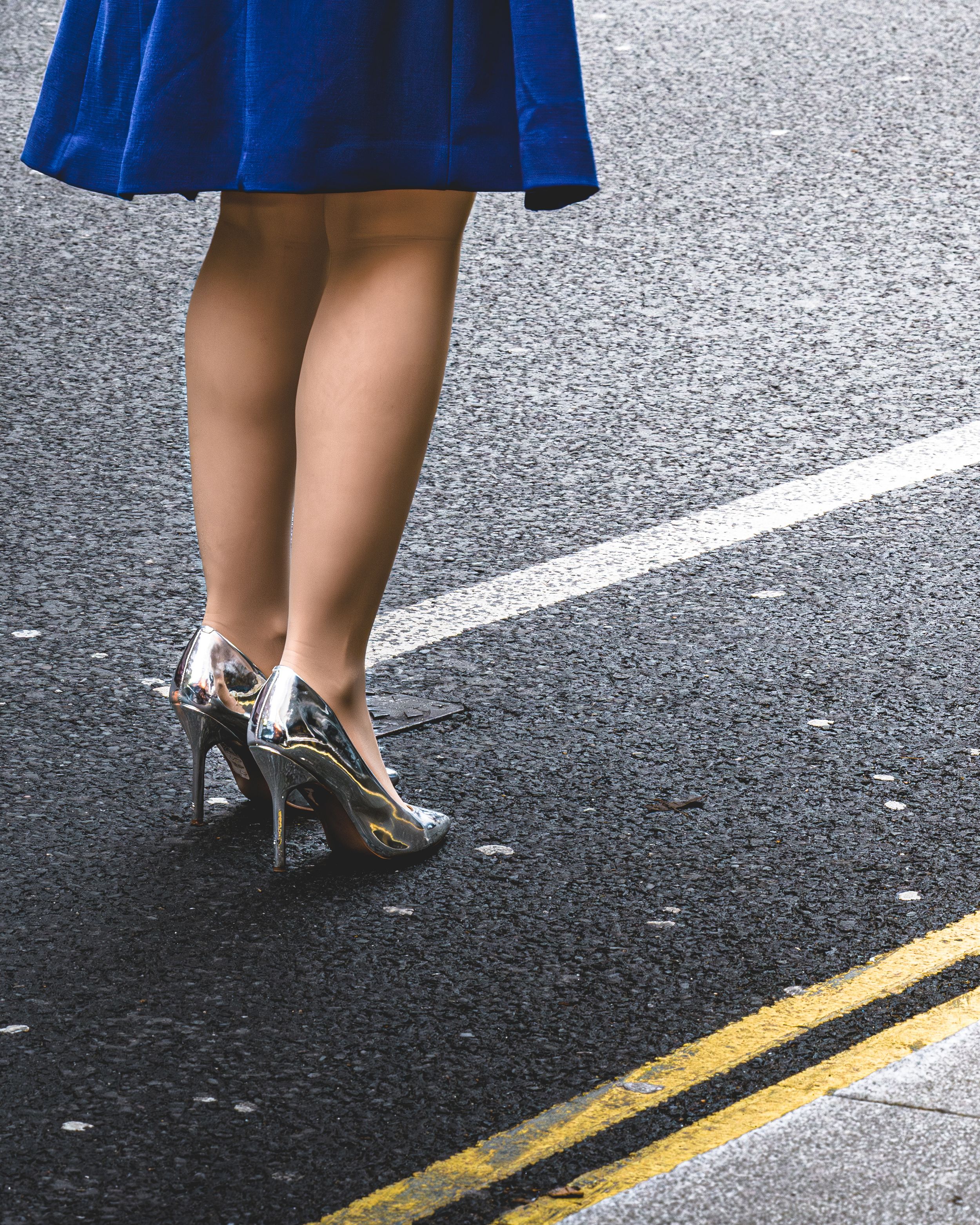 Street photography close-up of a woman's legs in a blue skirt and heels crossing the street