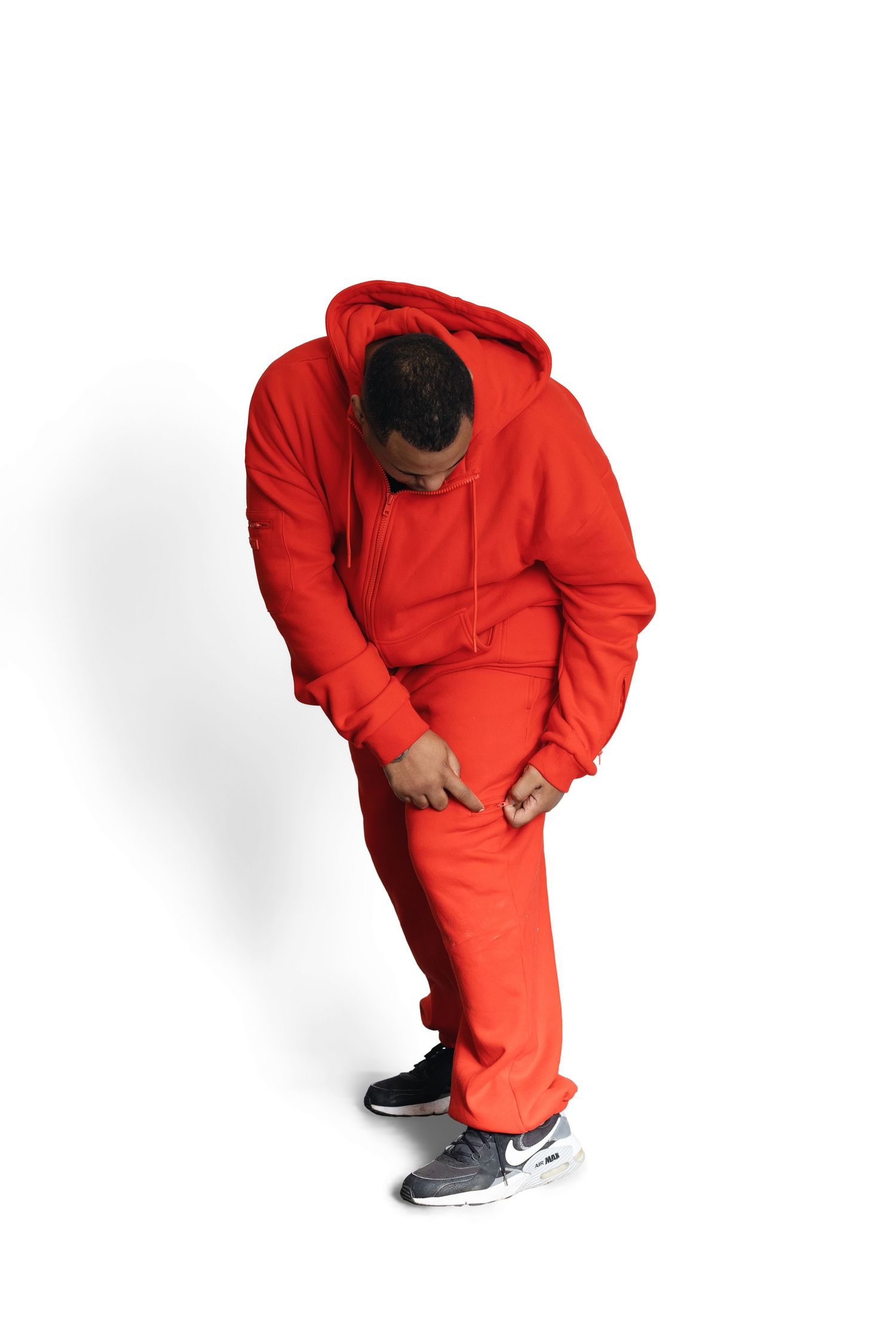 Man in red hoodie and sweatpants bending forward, wearing Nike sneakers, on white background.