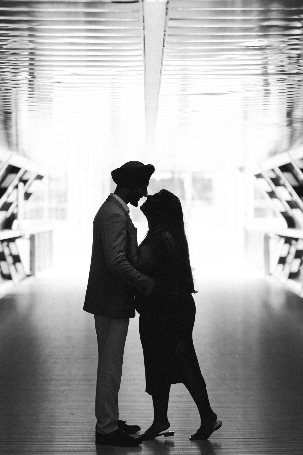 Black and white silhouette of a romantic couple sharing an intimate moment in a bright corridor.