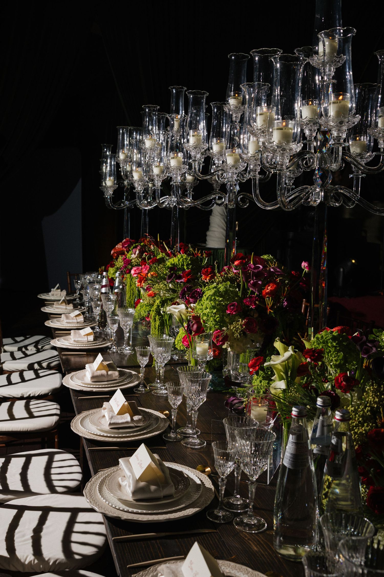 Elegant dinner table with crystal candelabras, red floral centerpieces, fine china, and crystal glassware set for a formal event.