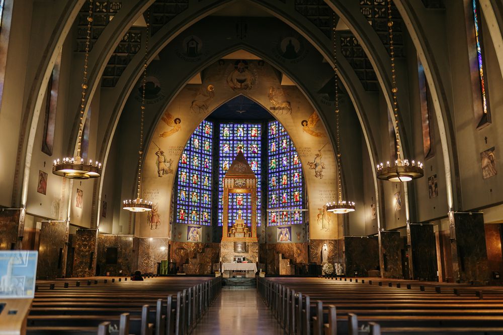 Grand cathedral interior with ornate stained glass windows, wooden pews, and Byzantine-style murals above the altar.