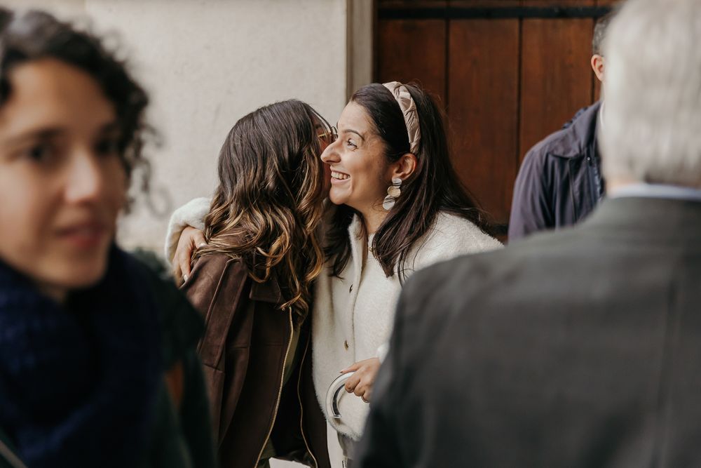 Two women smiling and whispering at a social gathering indoors.