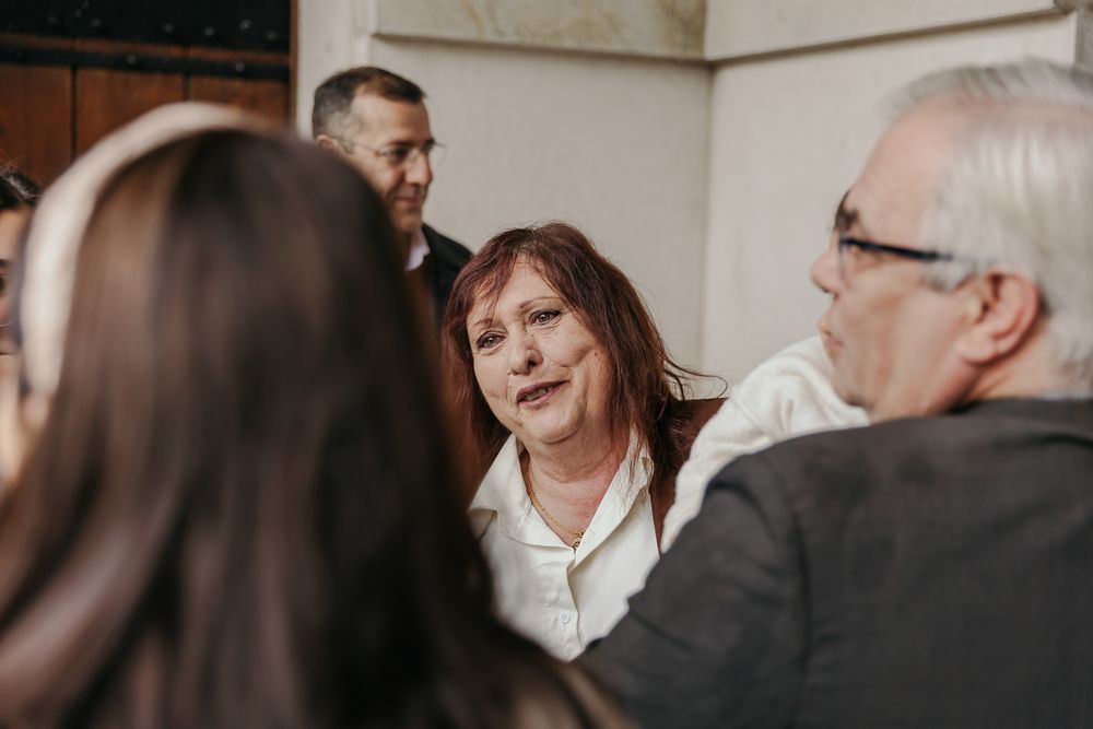 Woman with red hair in white jacket engaged in conversation at a social gathering with other attendees.