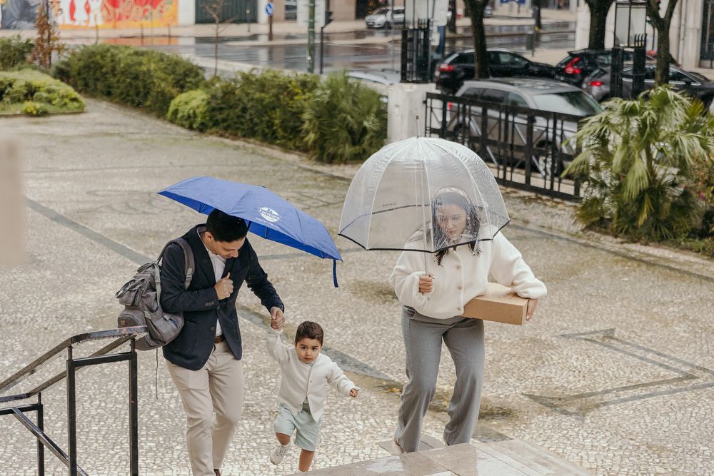 Family of three walking up steps in rain, adults holding blue and clear umbrellas while child runs ahead.