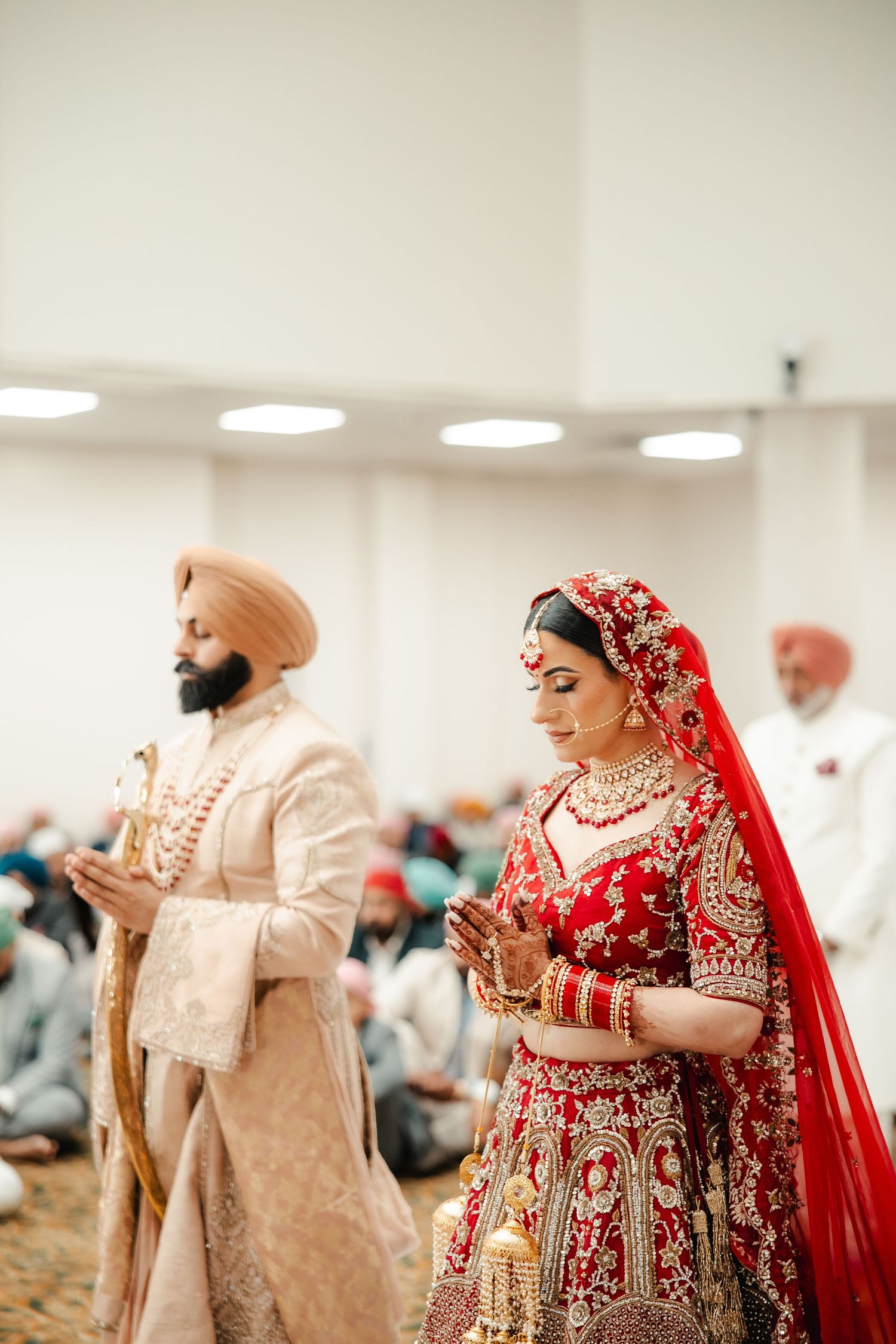 Sikh bride in red lehenga and groom in ivory sherwani perform traditional Anand Karaj wedding ceremony.