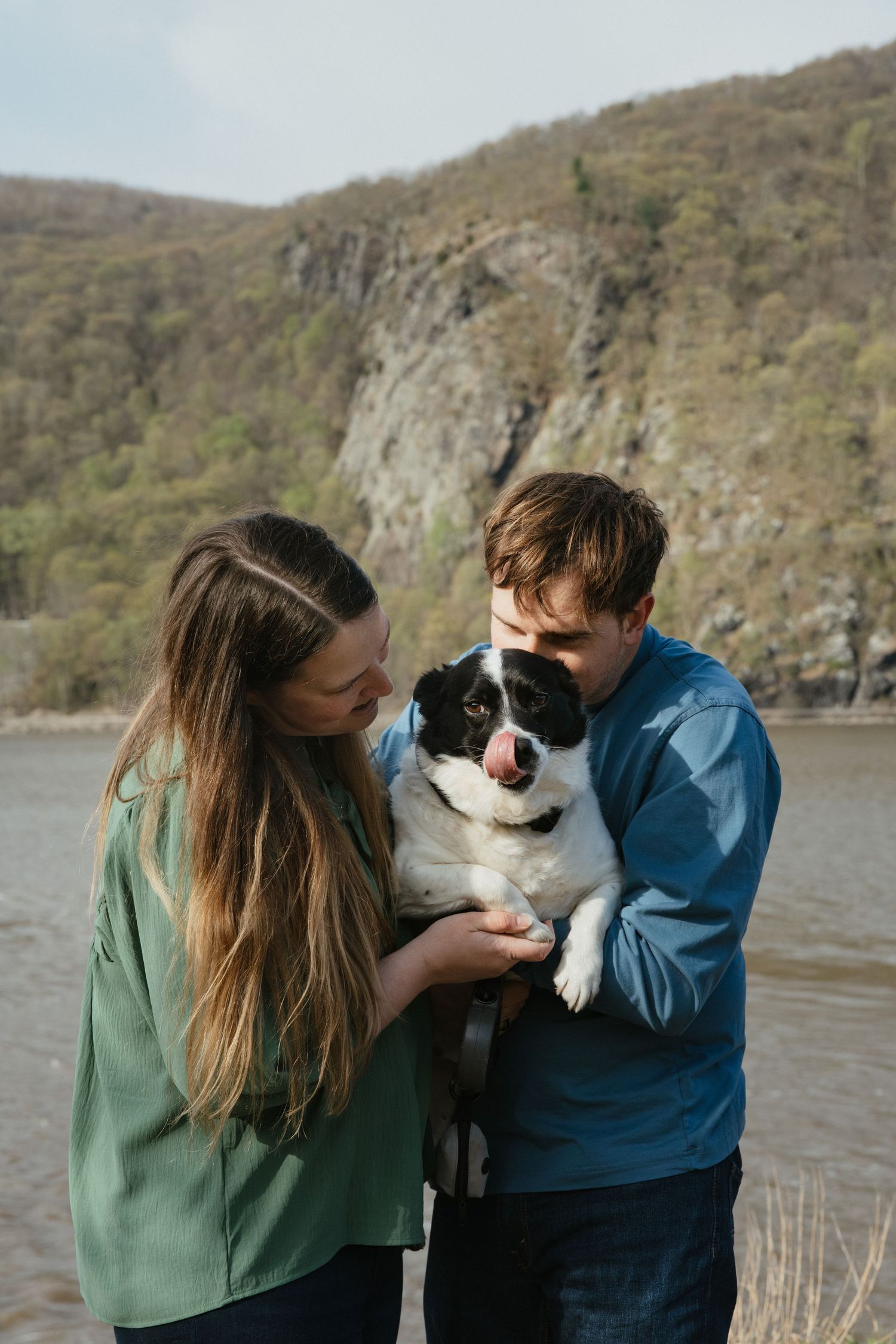 Couple embracing on a rocky cliff edge surrounded by trees under a dramatic cloudy sky.