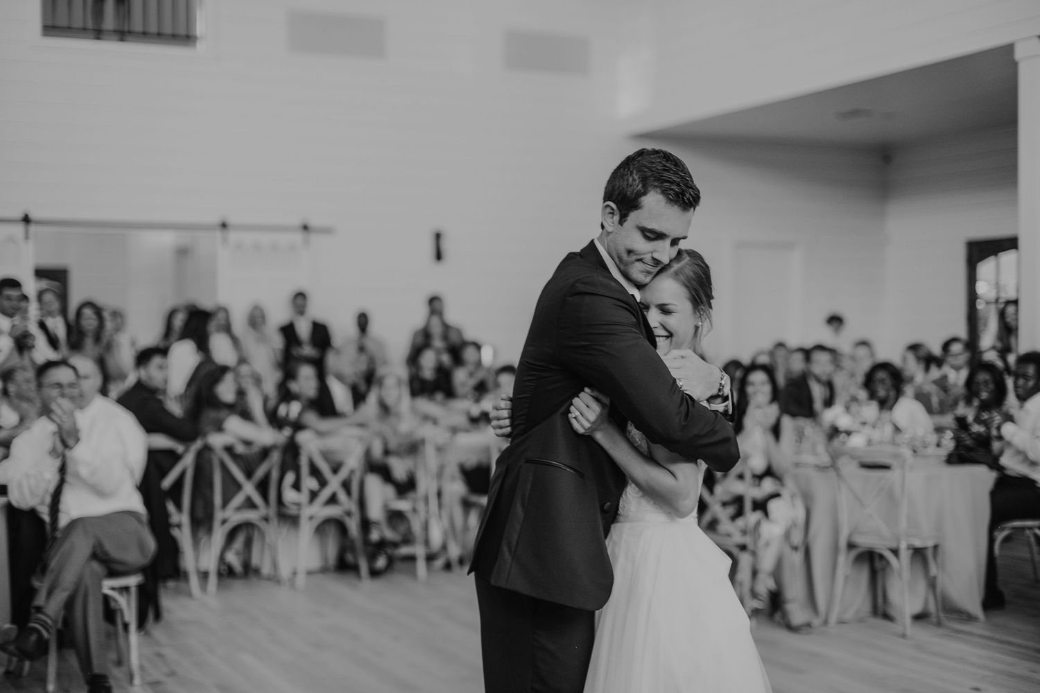 Bride and groom share their first dance at wedding reception with guests seated in background.