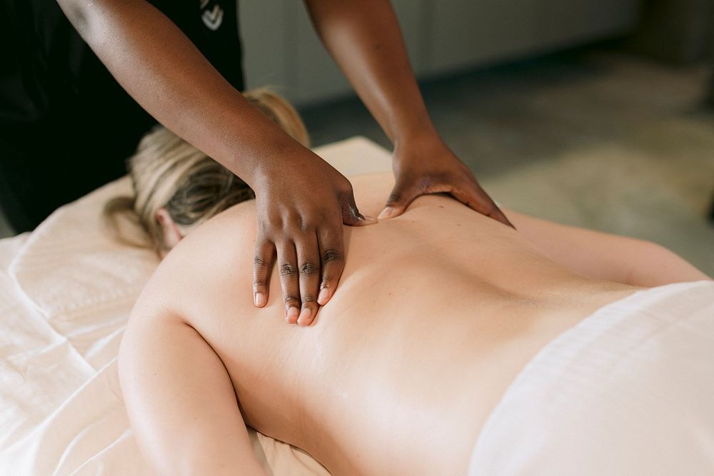 Professional massage therapist performing a relaxing back massage on a client lying on a white massage table.
