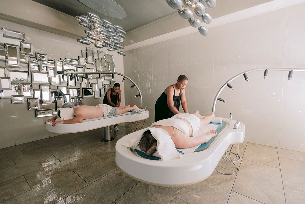 Luxury spa treatment room with futuristic floating bath pods and therapists providing relaxing water treatments.