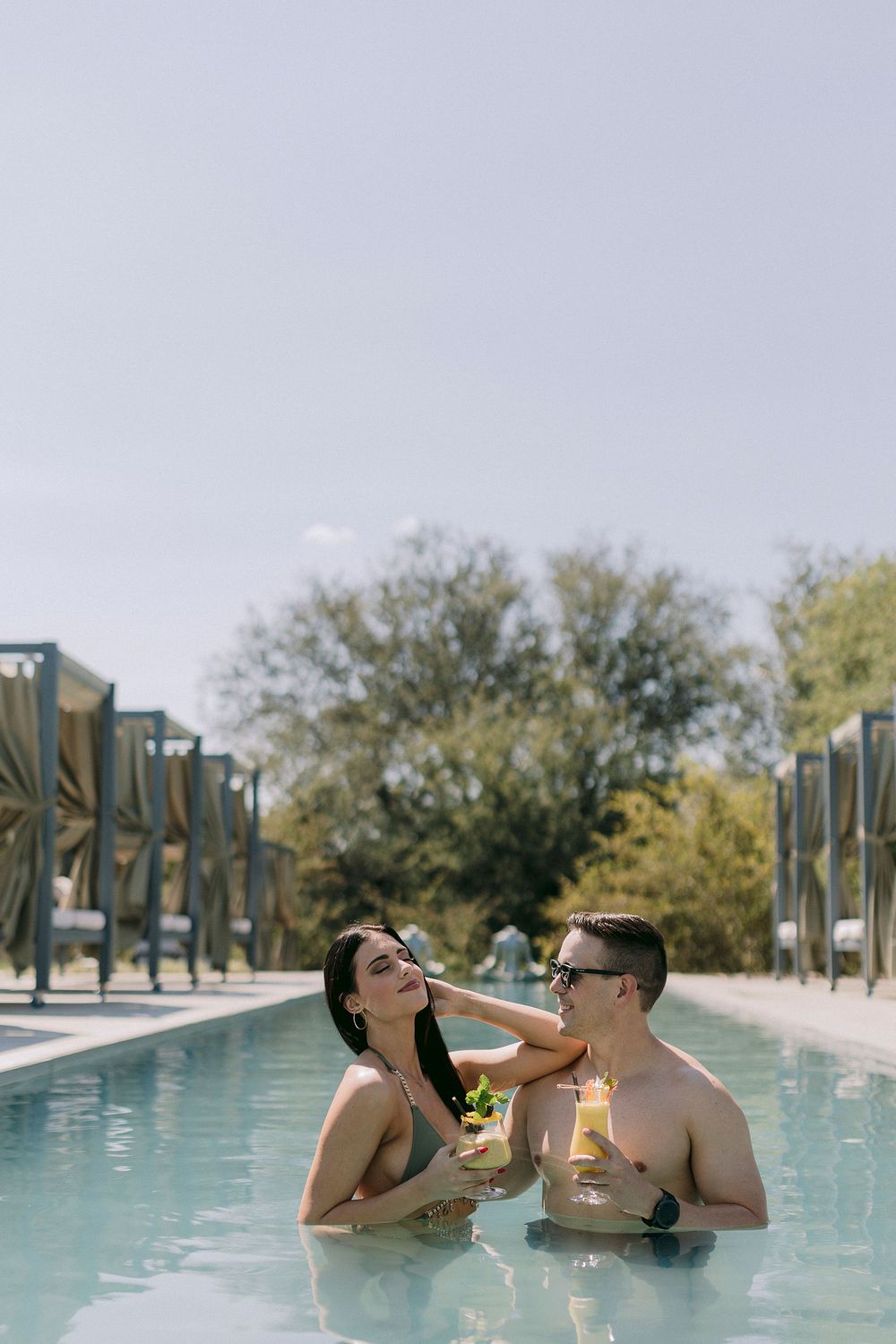 Couple enjoying cocktails together in a luxury outdoor swimming pool on a sunny day.