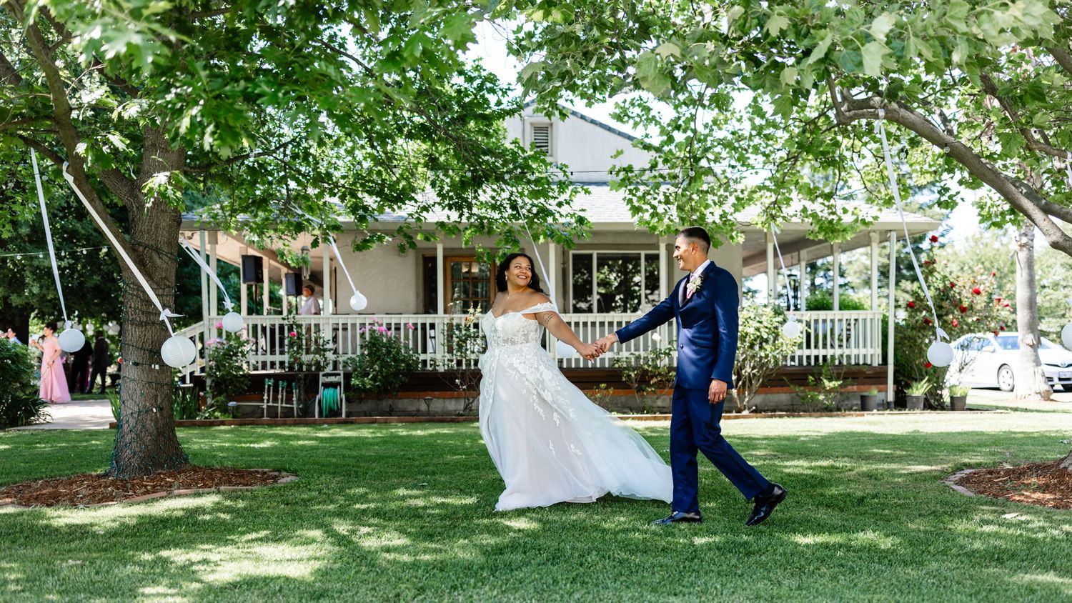 A joyful couple dance outdoors at their wedding with a white farmhouse and trees in the background.