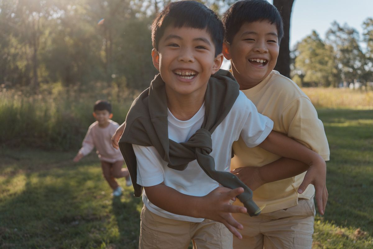 Three Asian boys playing outdoors in a sunny park, two smiling brothers hugging in the foreground. family photoshoot in rouse hill sydney