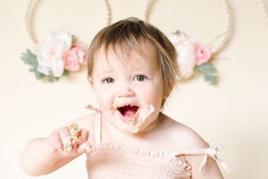Cute baby girl with frosting on her face enjoying her first birthday cake smash photo session.