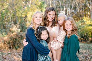 Mother smiling with four daughters outdoors among colorful fall foliage.