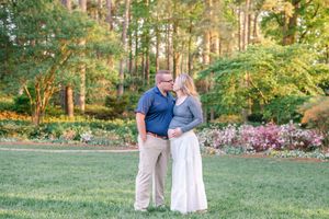 An expectant couple shares a tender kiss while standing in a colorful garden at golden hour.