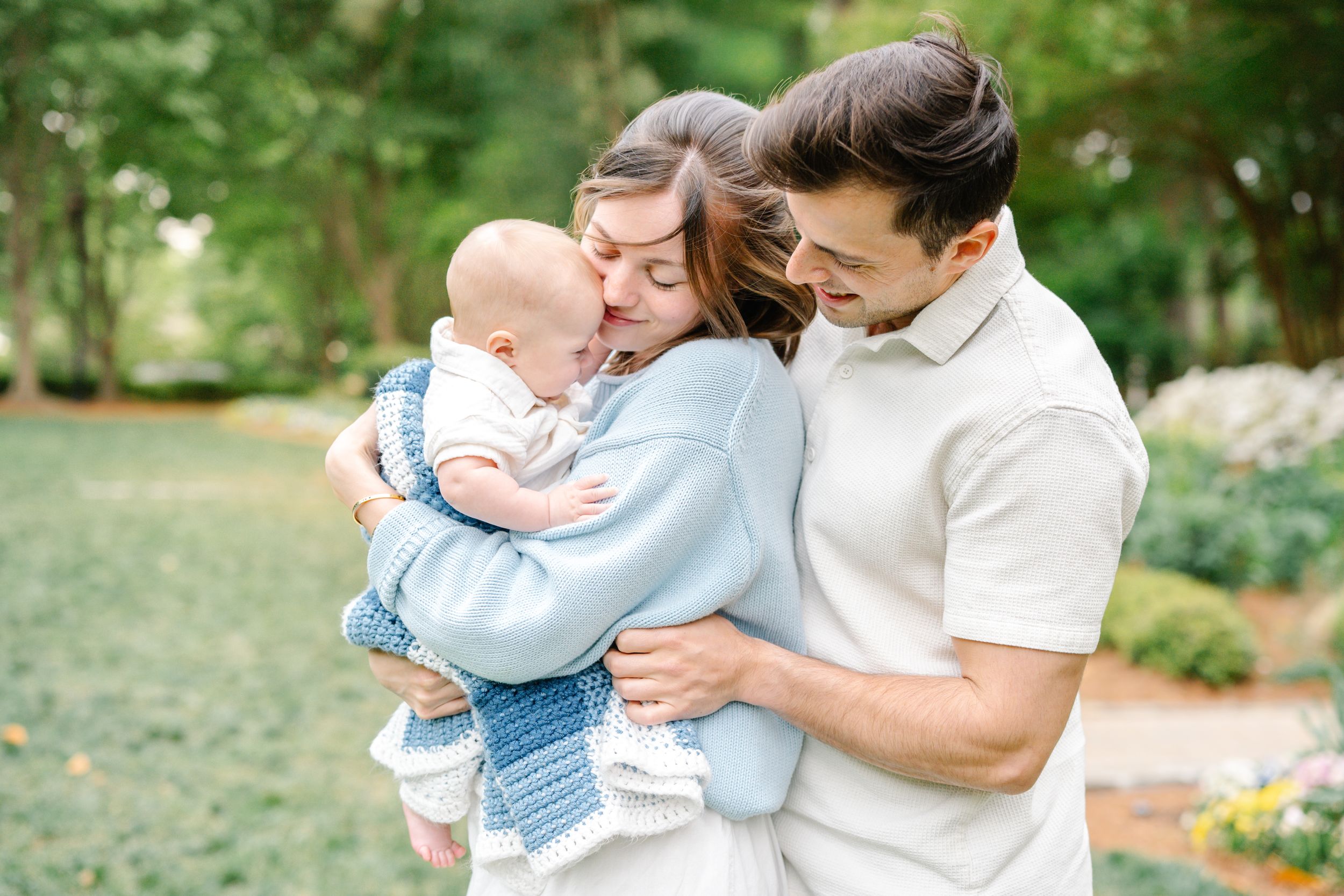 Happy young family sharing a joyful moment together with their laughing baby outdoors in a garden.