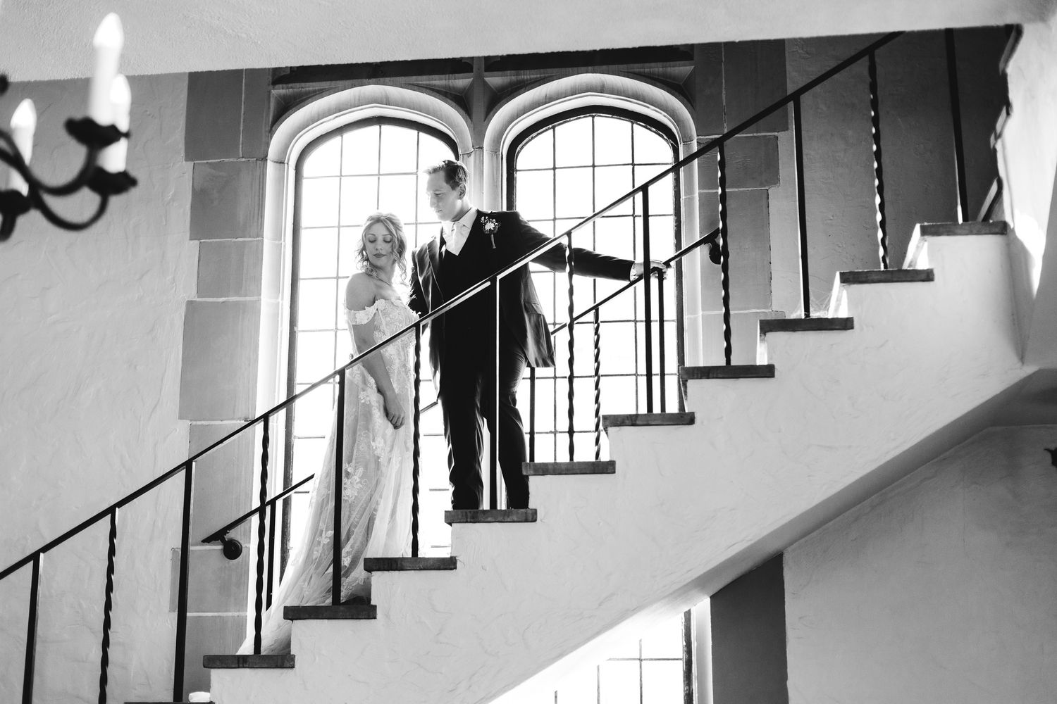 Bride and groom share a romantic moment on an elegant staircase in black and white photo.