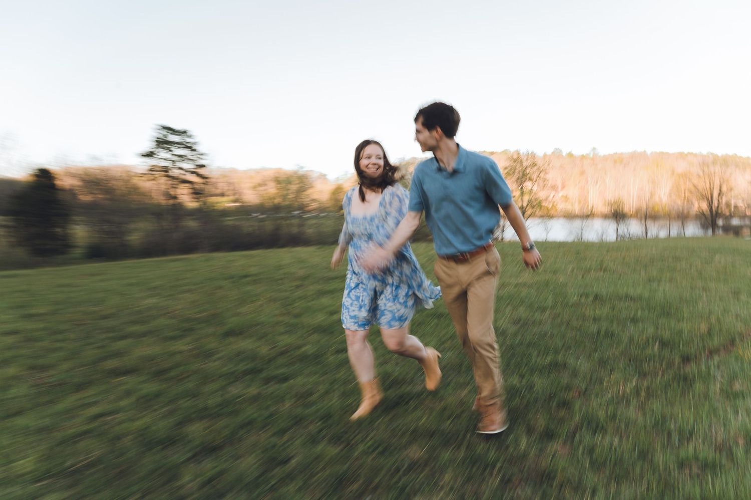 A joyful couple runs hand-in-hand through a lush green field at sunset, smiling and enjoying a carefree moment outdoors.
