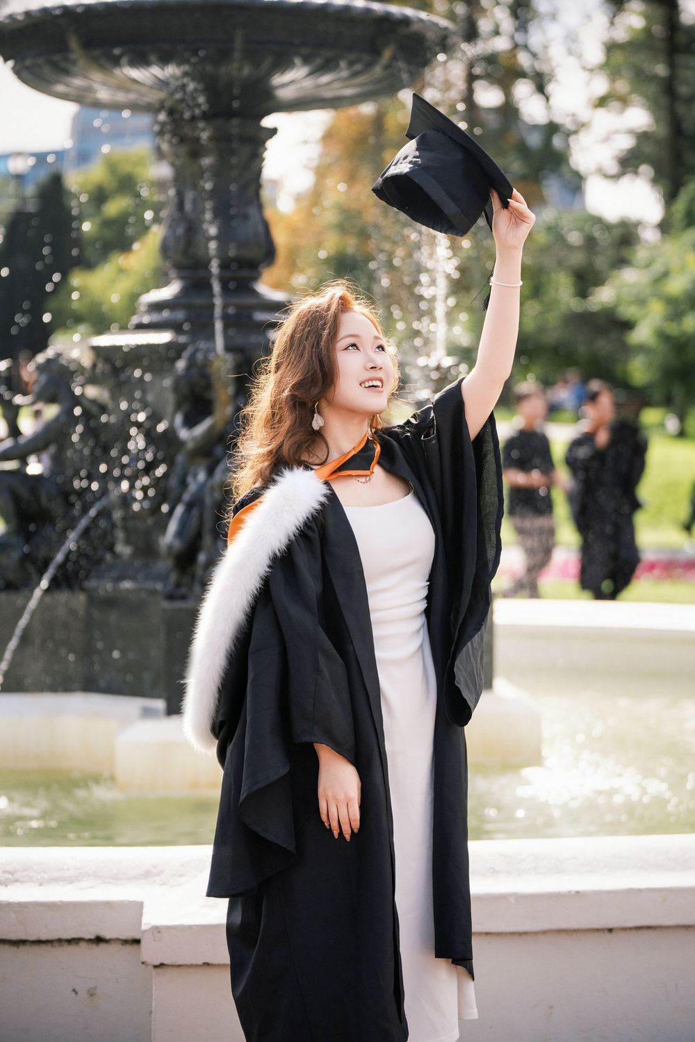 Happy student celebrating her academic achievement by the famous historic fountain in Albert Park, Auckland.