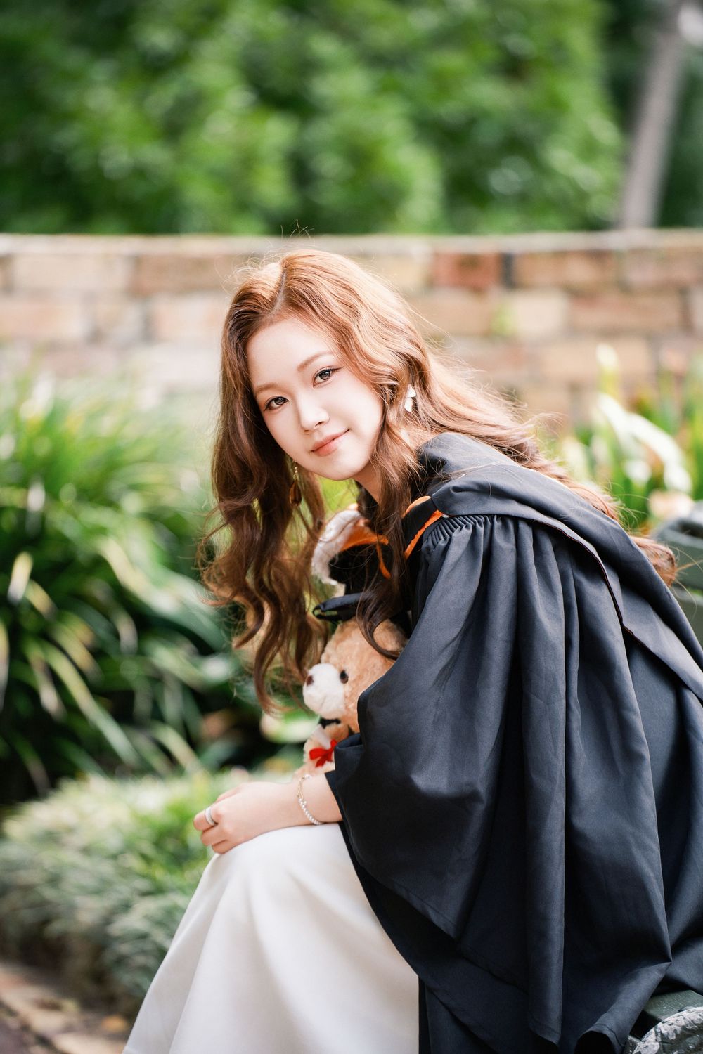 Natural outdoor graduation photo of a female student smiling in a lush park near UoA.