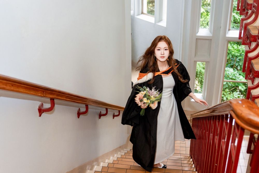 Beautiful indoor graduation photos of a student in regalia on the grand stairs of the historic UoA Clock Tower.