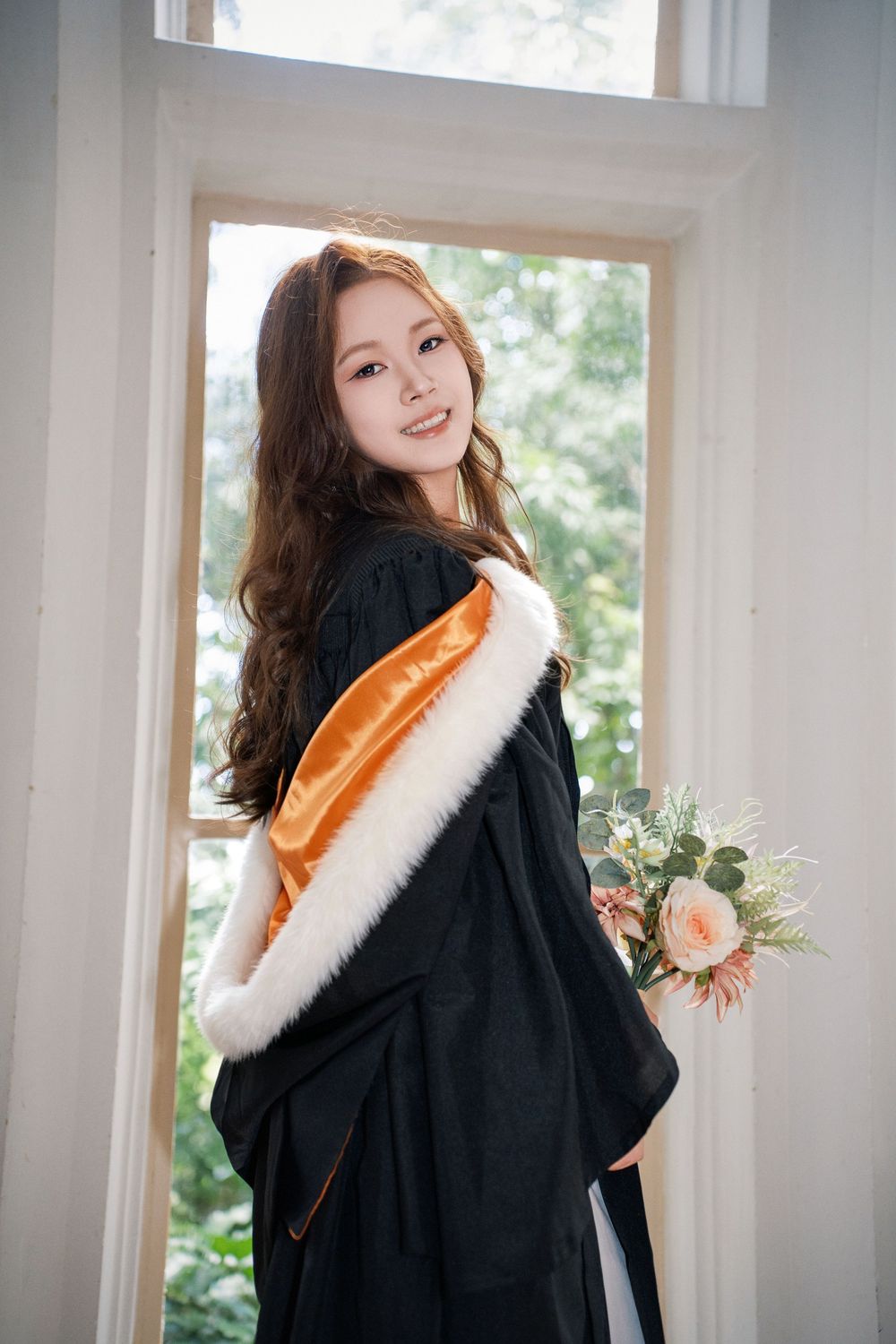 Beautiful indoor portrait of a graduate next to a classic window inside the historic UoA Clock Tower.