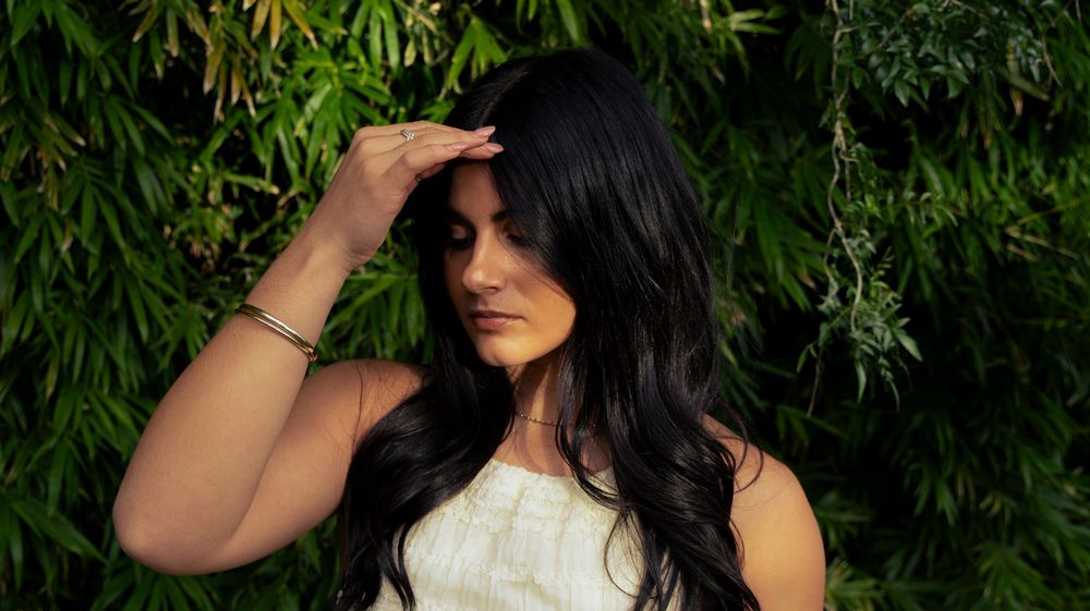 Young woman with long black hair in white dress posing against lush green bamboo foliage.