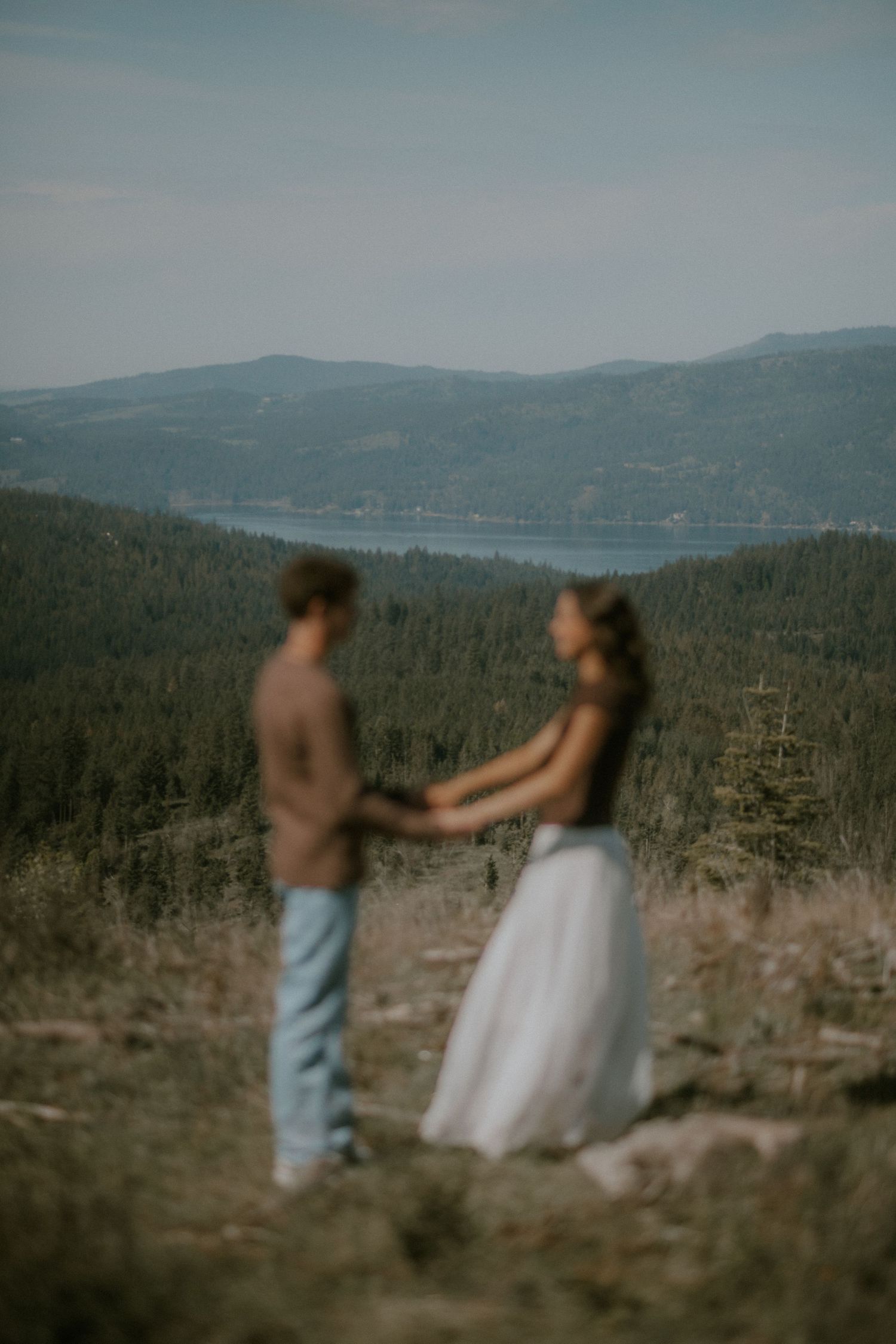 Couple holding hands during outdoor elopement ceremony with mountain lake and forest backdrop.