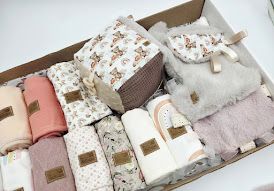 Pink baby gift box set with floral blanket, booties, and accessories tied with a satin ribbon bow.