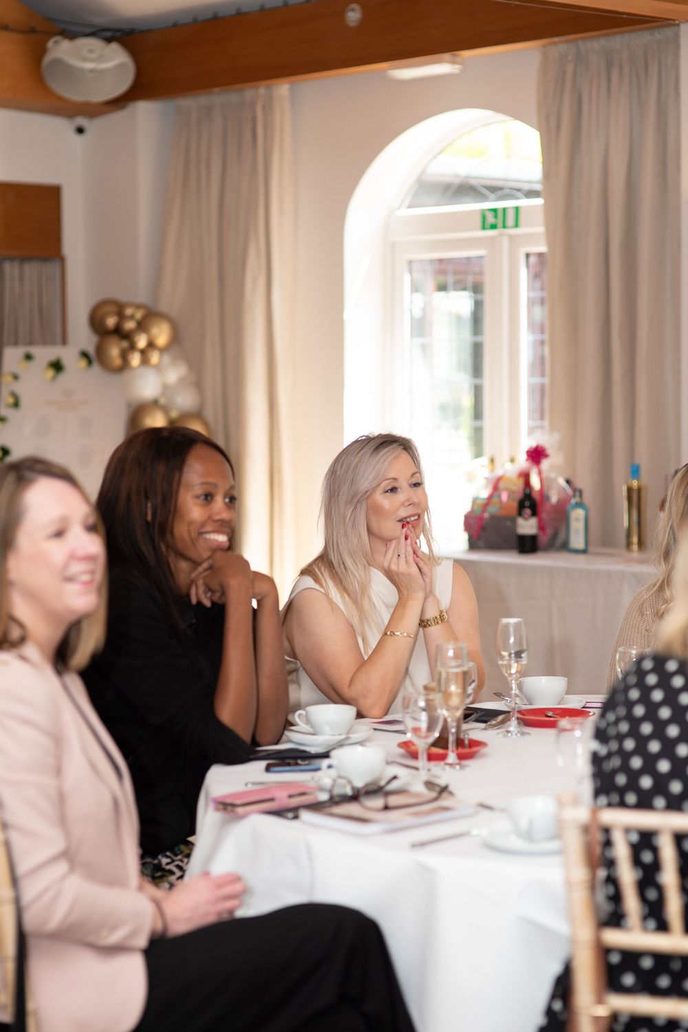 Women seated at a elegantly set table laughing and smiling at a formal luncheon event in a bright venue.