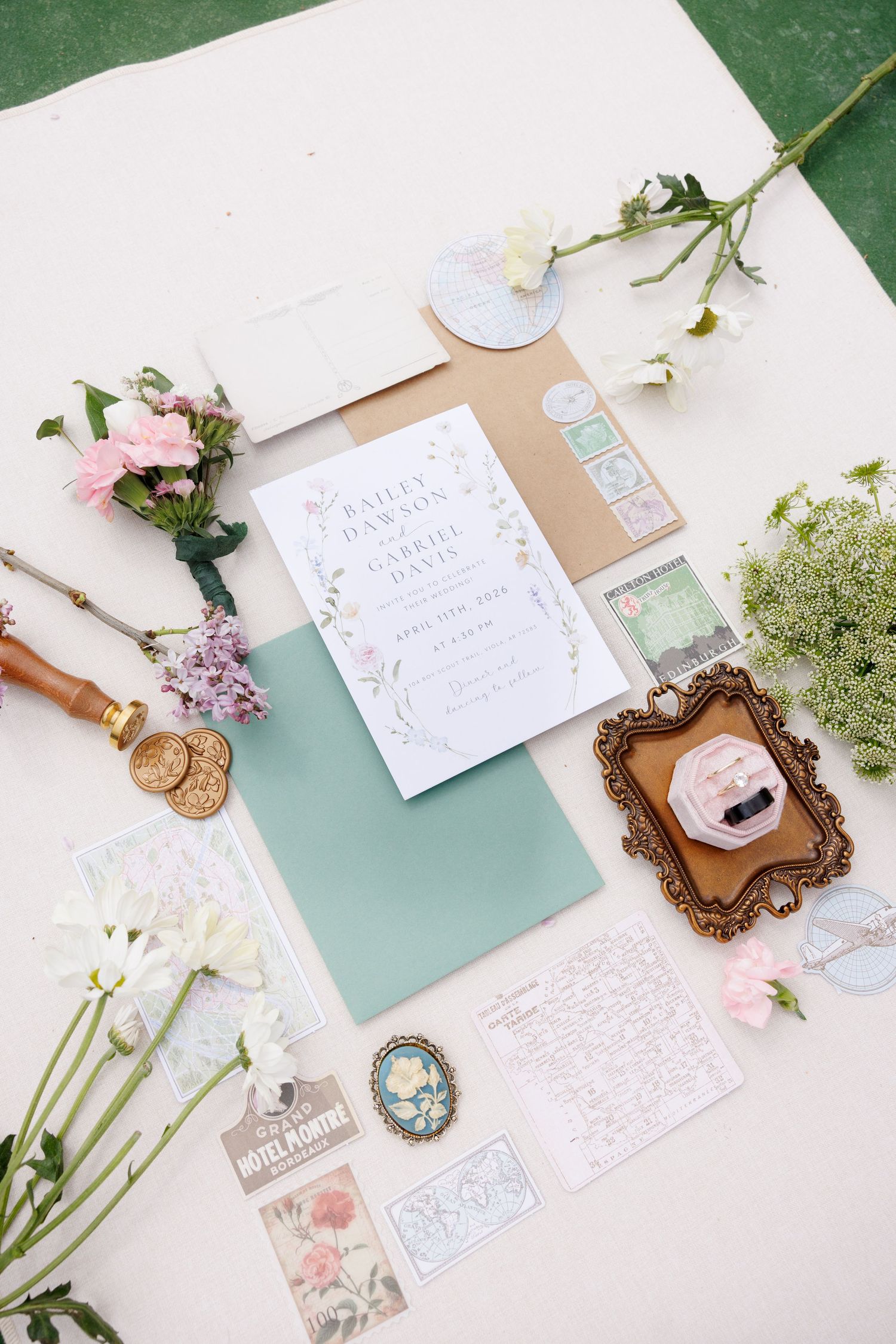 Elegant wedding invitation suite flatlay with pastel florals, mint envelopes, vintage brooch, and decorative stationery.