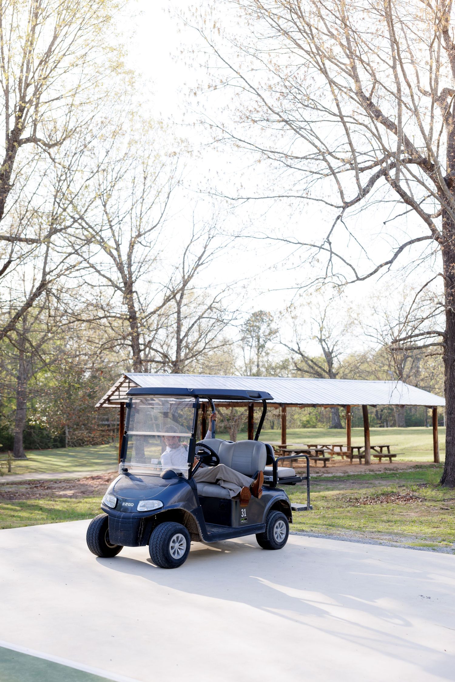 A navy blue golf cart parked on a paved path surrounded by tall trees at an outdoor wedding venue.