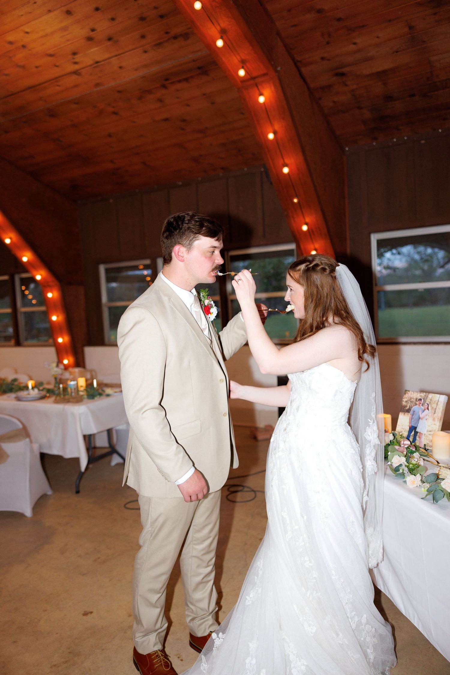 Bride and groom share a romantic first dance in a rustic barn wedding venue decorated with warm string lights.