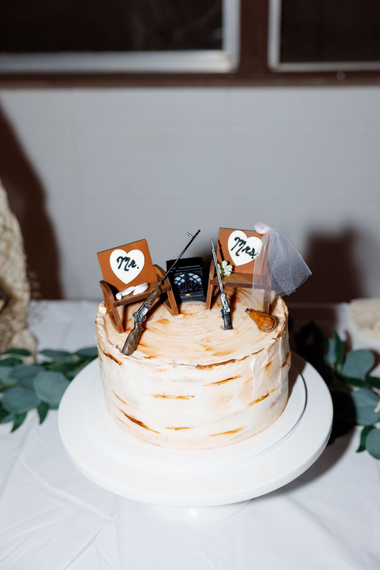 Rustic wedding cake with Mr. and Mrs. hunting chair toppers and a radio, frosted in textured white buttercream.
