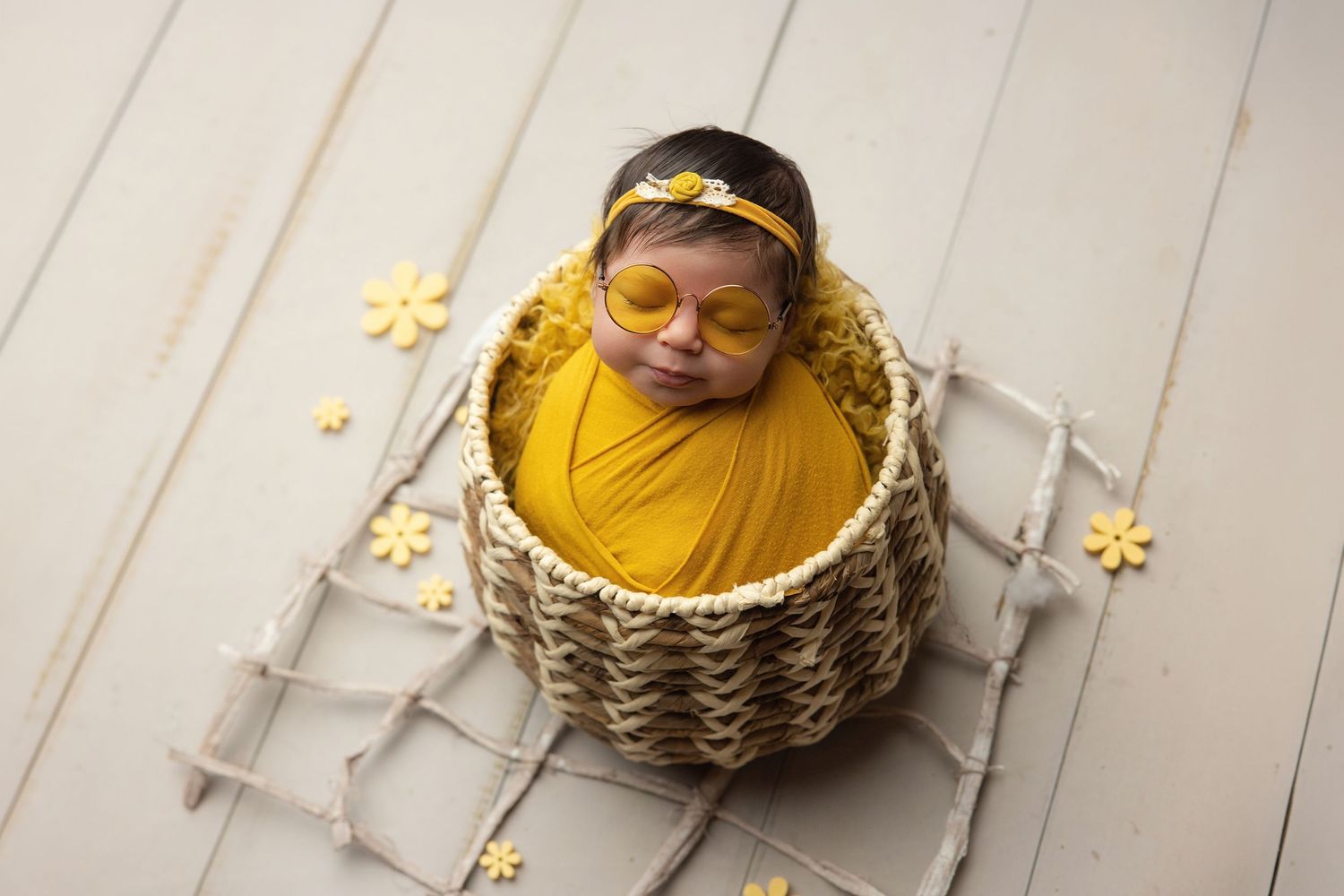 Newborn baby wrapped in teal swaddle holding green knit bear toy, resting in decorative bucket.