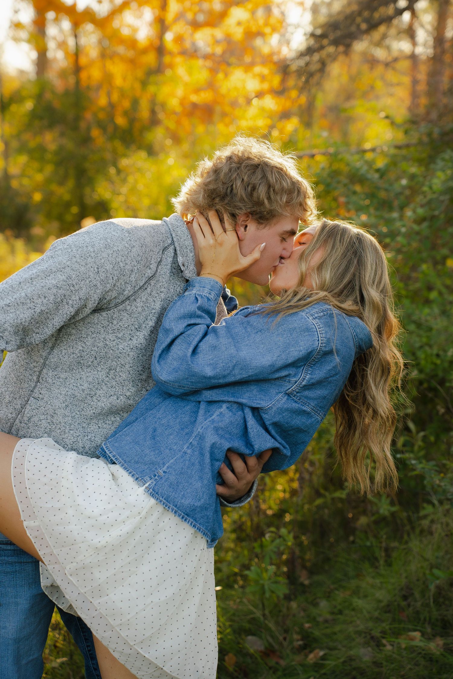 Couple sharing a romantic moment on a wooden dock by a lake with autumn foliage in the background.