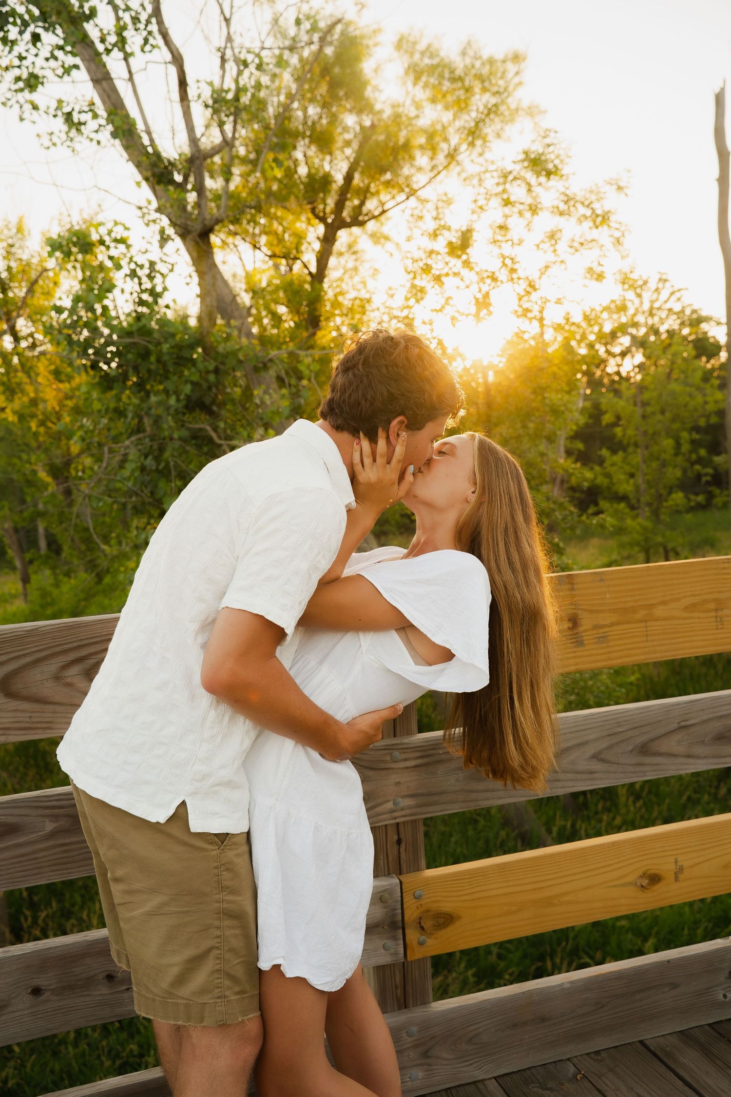 Couple sharing a romantic moment on a wooden dock by a lake with autumn foliage in the background.