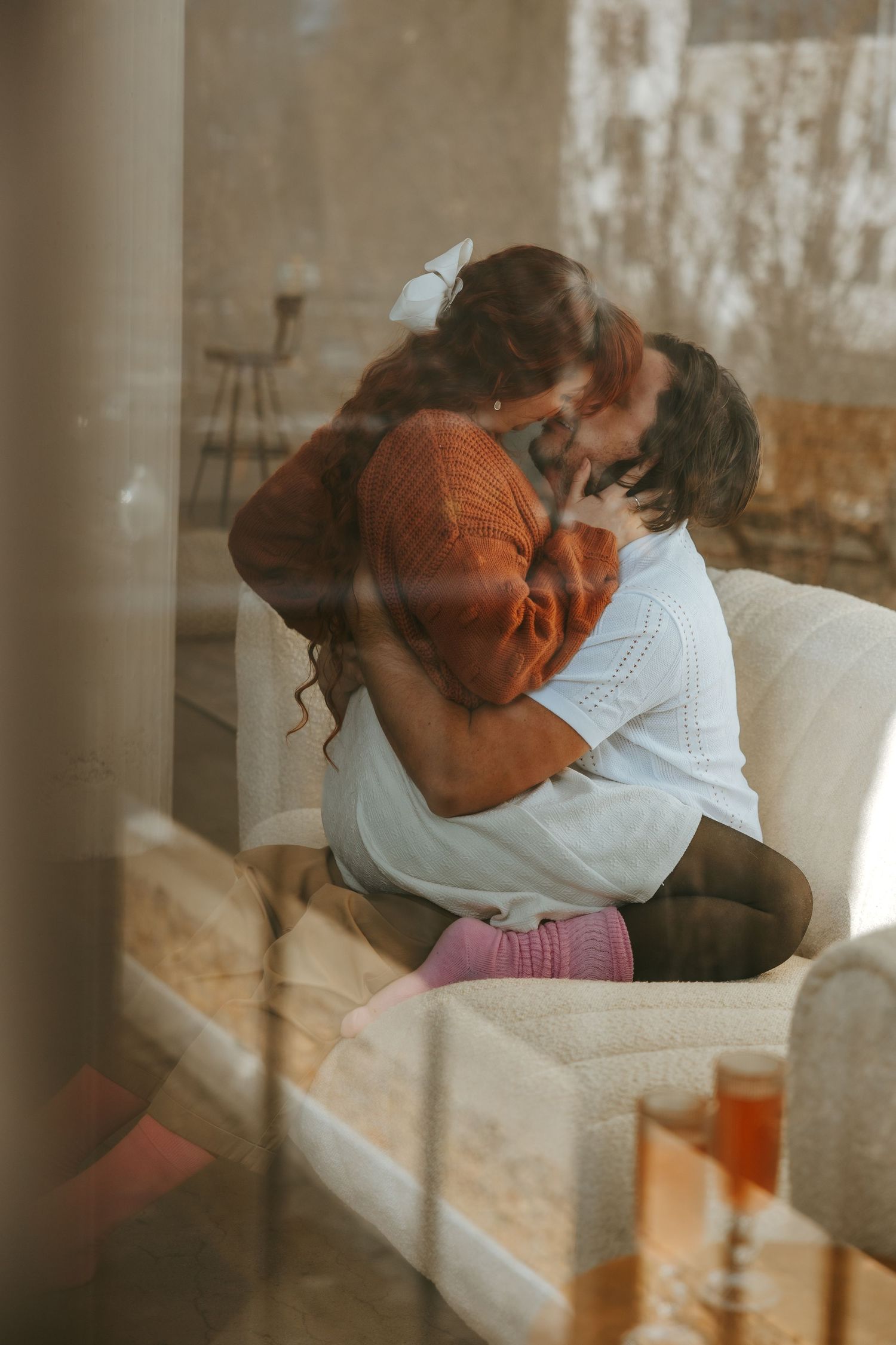 A romantic embrace on a cozy couch with warm sunlight streaming through windows.